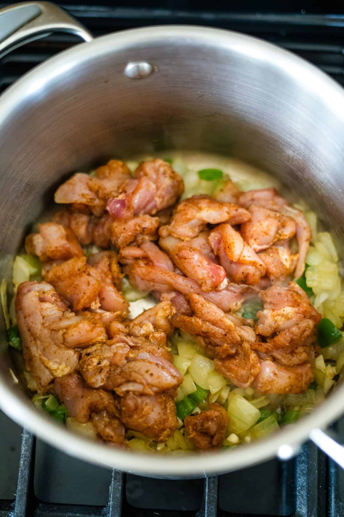 Chunks of seasoned meat simmer alongside onions and green peppers, infusing the stainless steel pot with flavors reminiscent of a hearty chicken chipotle soup.