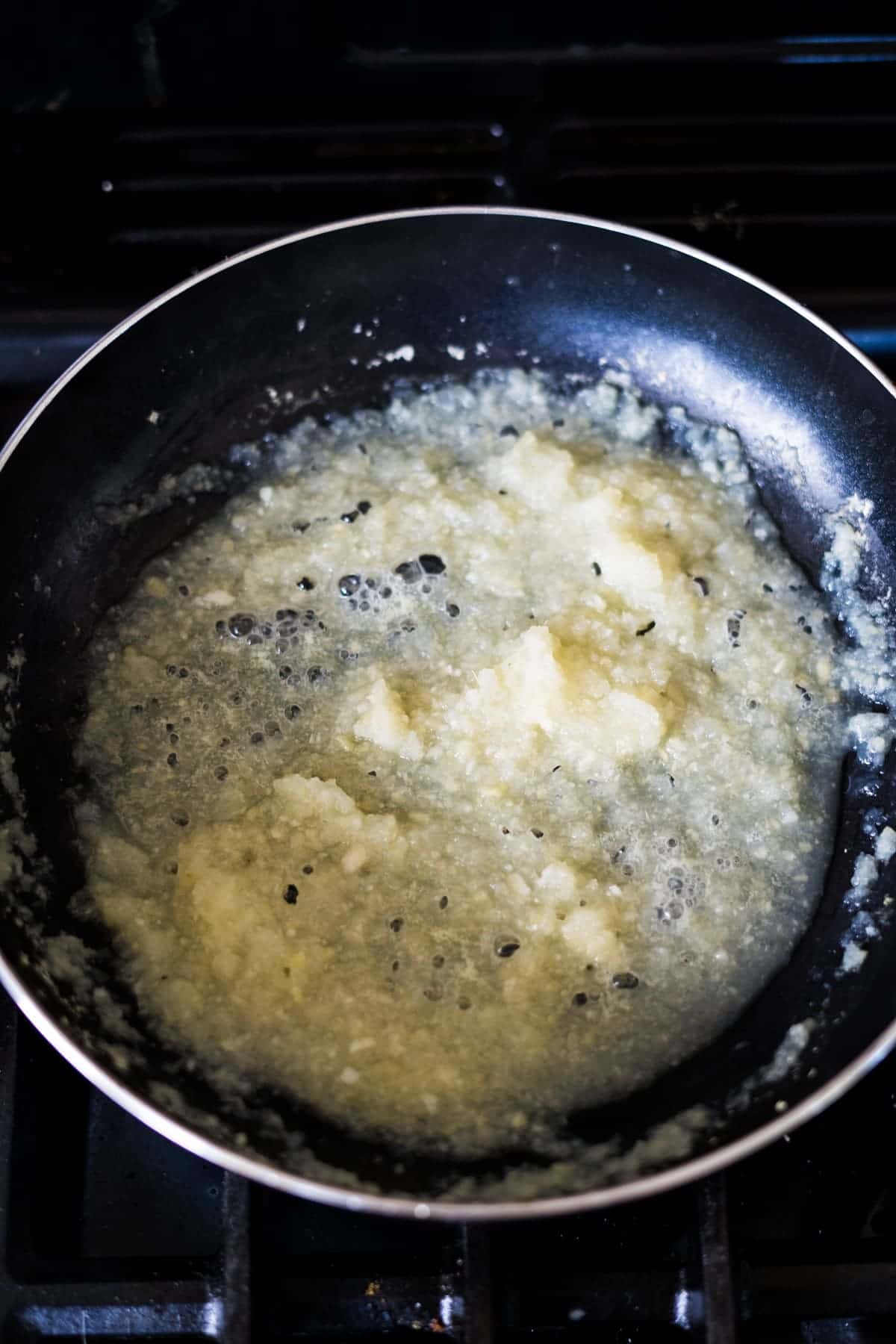 A frying pan on a stove contains bubbling onions sautéing in oil.