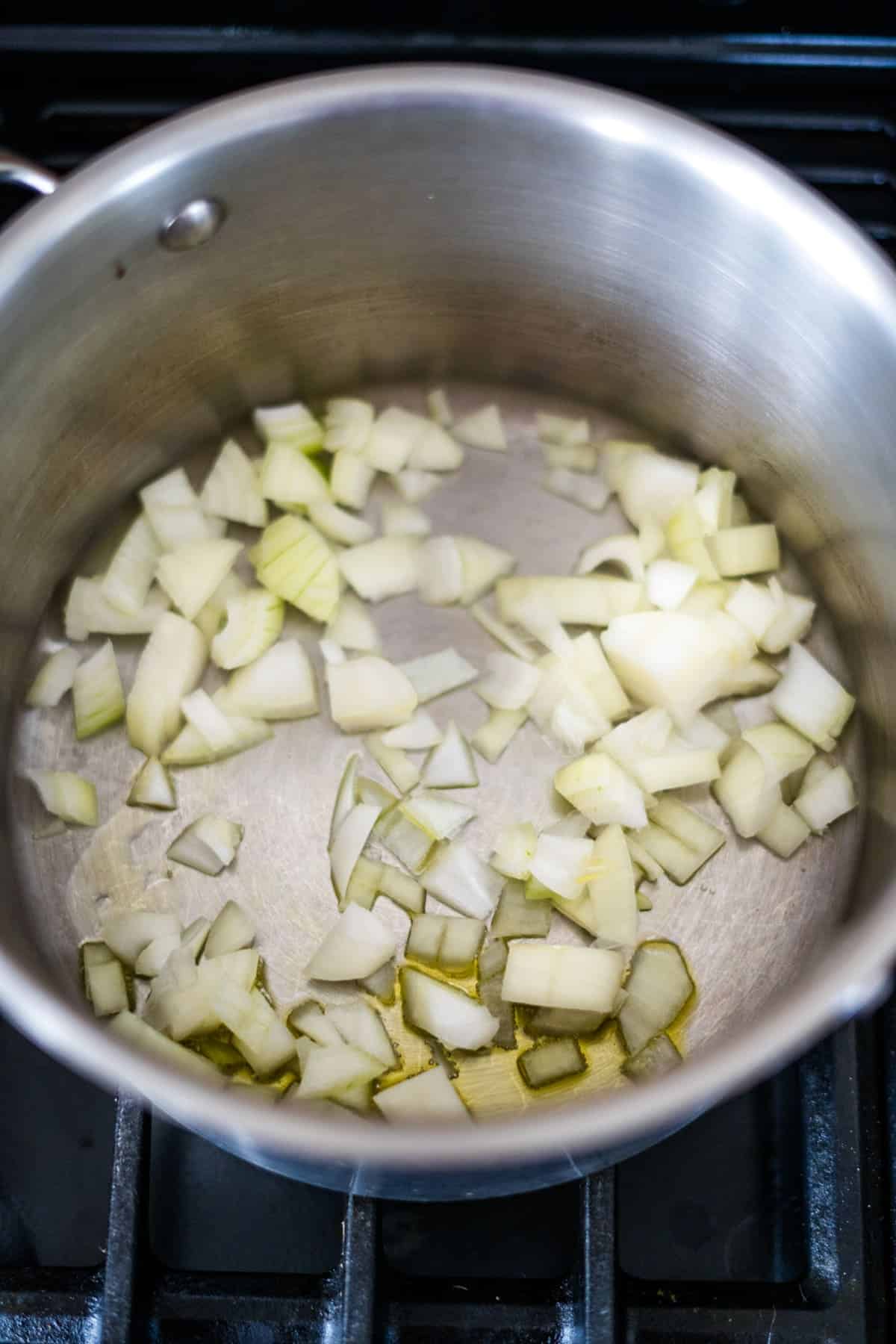 Chopped onions sautéing in a stainless steel pot with a small amount of oil on the stovetop form the aromatic base for a savory chicken chipotle soup.