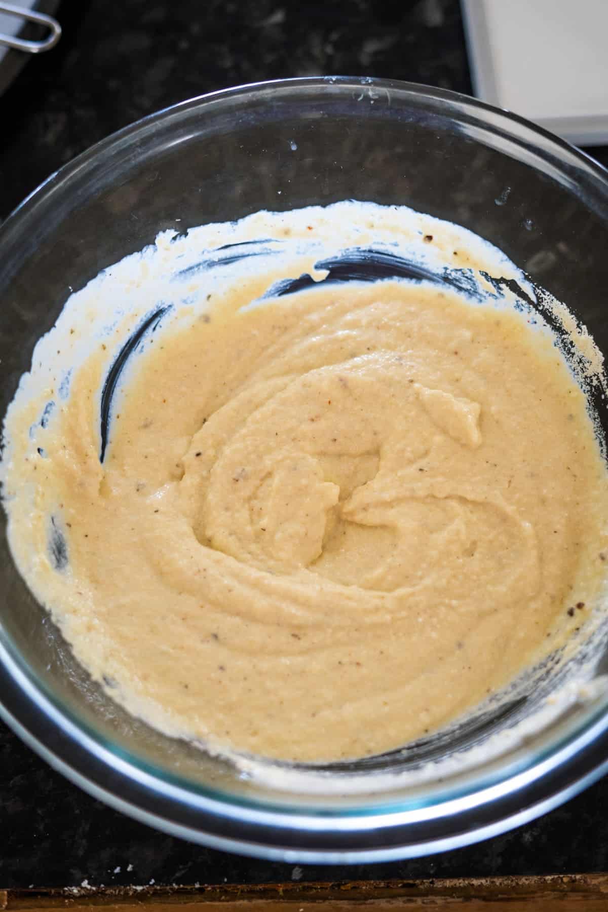 A glass bowl filled with smooth, creamy batter on a dark countertop.