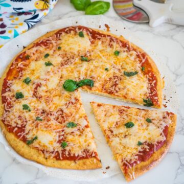 A cheese pizza with tomato sauce and basil leaves, missing one slice, on a white surface.