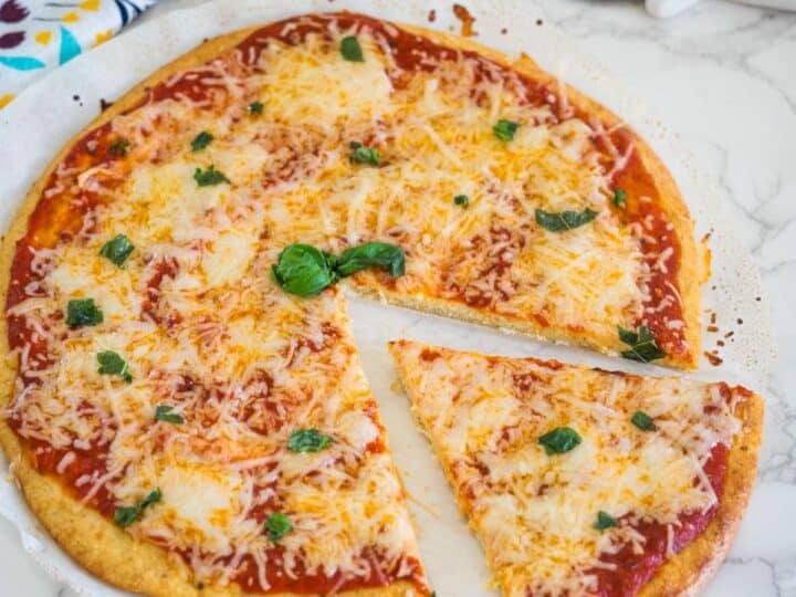 A cheese pizza with tomato sauce and basil leaves, missing one slice, on a white surface.