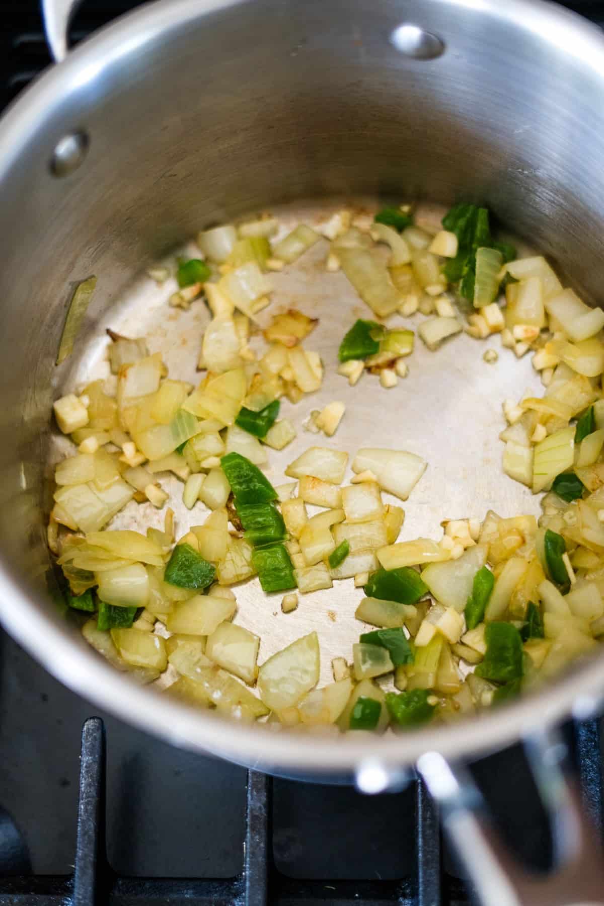 Diced onions and green peppers sautéing in a stainless steel pot on the stove create the perfect foundation for a flavorful chicken chipotle soup.