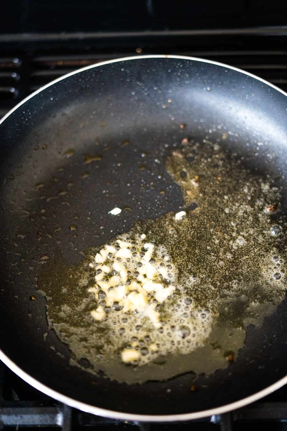 Chopped garlic sizzling in heated oil in a black frying pan.