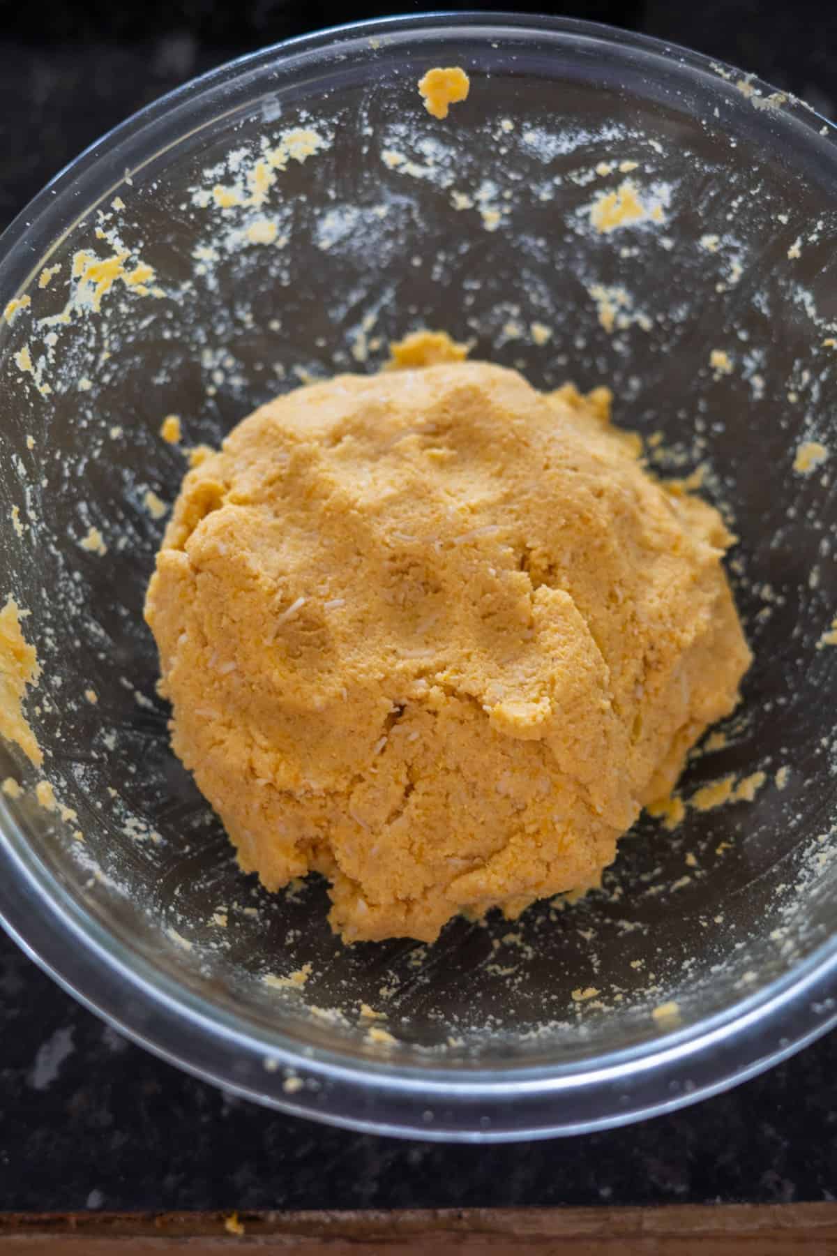 A ball of yellow dough in a clear glass bowl on a black countertop.