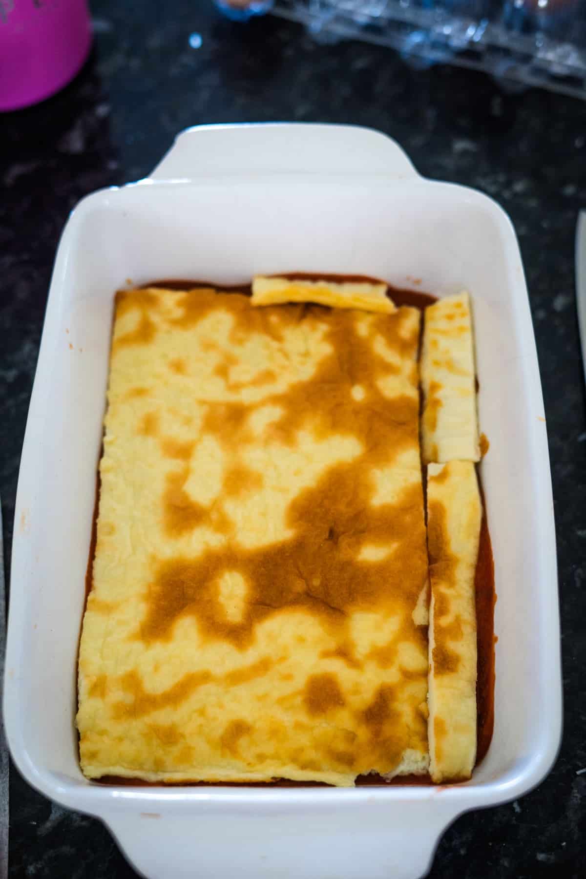 A delicate keto spinach lasagna, featuring a rectangular baked dish with a golden-brown top and uneven edges, all beautifully presented in a white ceramic baking pan.