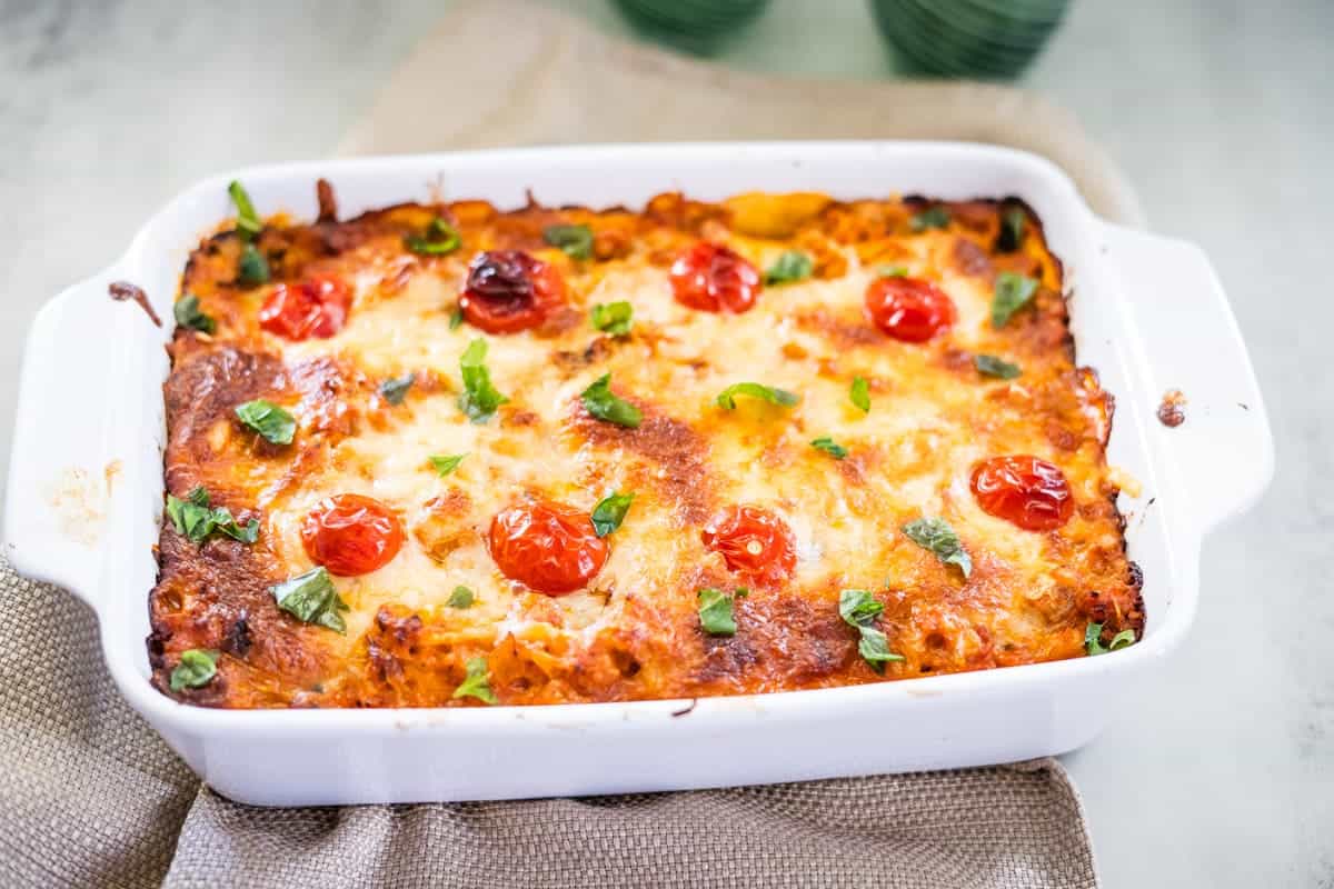 A delightful spaghetti squash pizza casserole in a white dish, topped with melted cheese, cherry tomatoes, and fresh herbs.