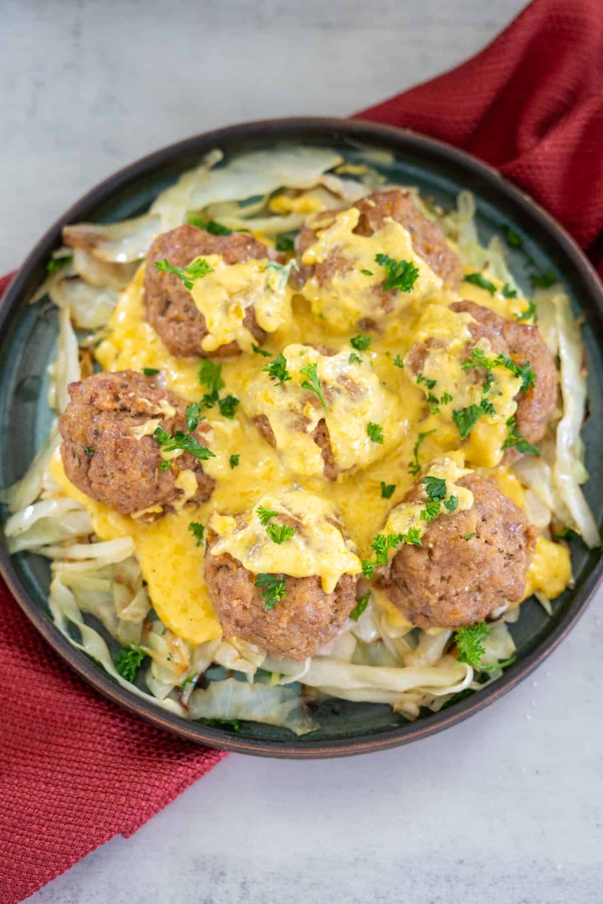 Plate of meatballs covered in yellow sauce, garnished with chopped herbs, served on a bed of shredded cabbage. A red napkin lies beside the plate.