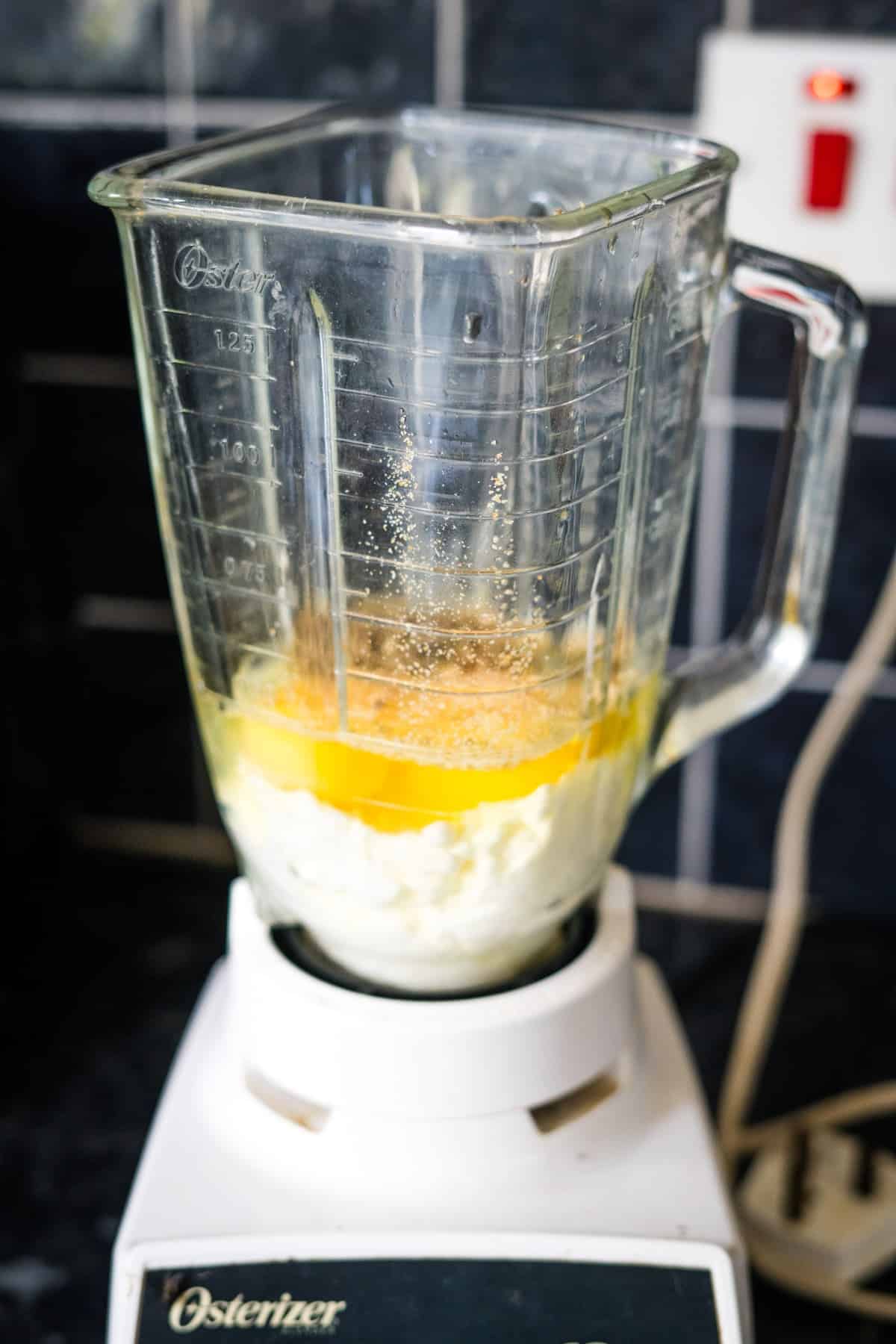 A blender on a counter contains eggs, flour, sugar, and other ingredients, ready for mixing.