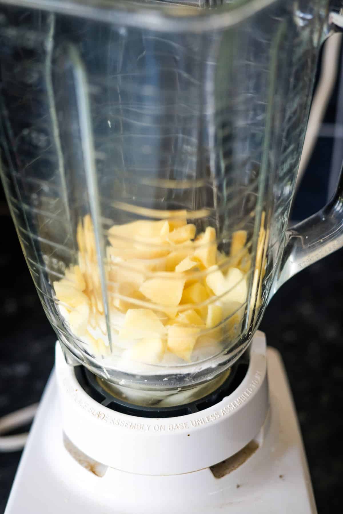 Chopped ginger pieces in a glass blender jar on a white base.