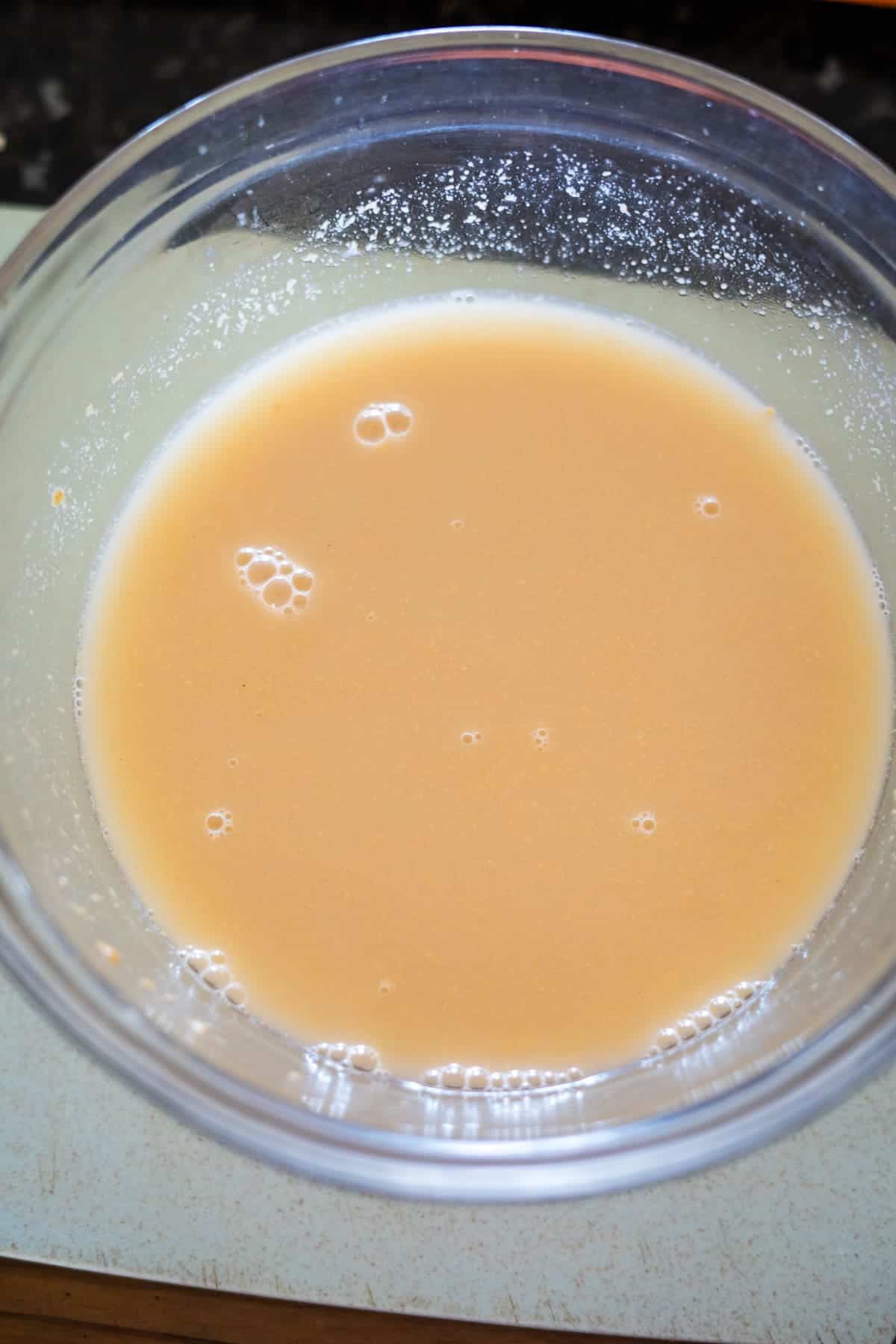 A clear bowl containing a light brown liquid with small bubbles on the surface, set on a light-colored table.