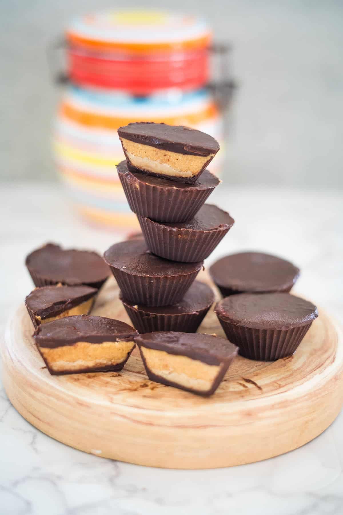 A stack of high protein peanut butter cups sits elegantly on a wooden plate, with a colorful jar in the background adding a vibrant touch.