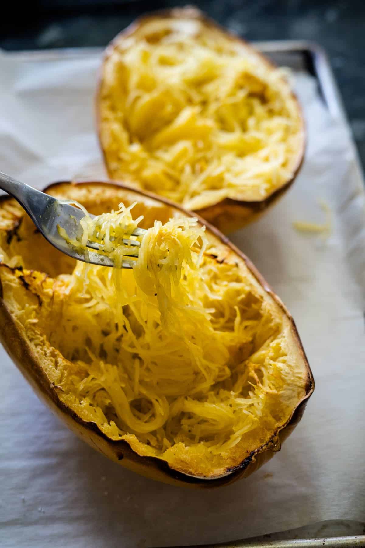 Fork pulling strands from a cooked spaghetti squash on a baking tray.