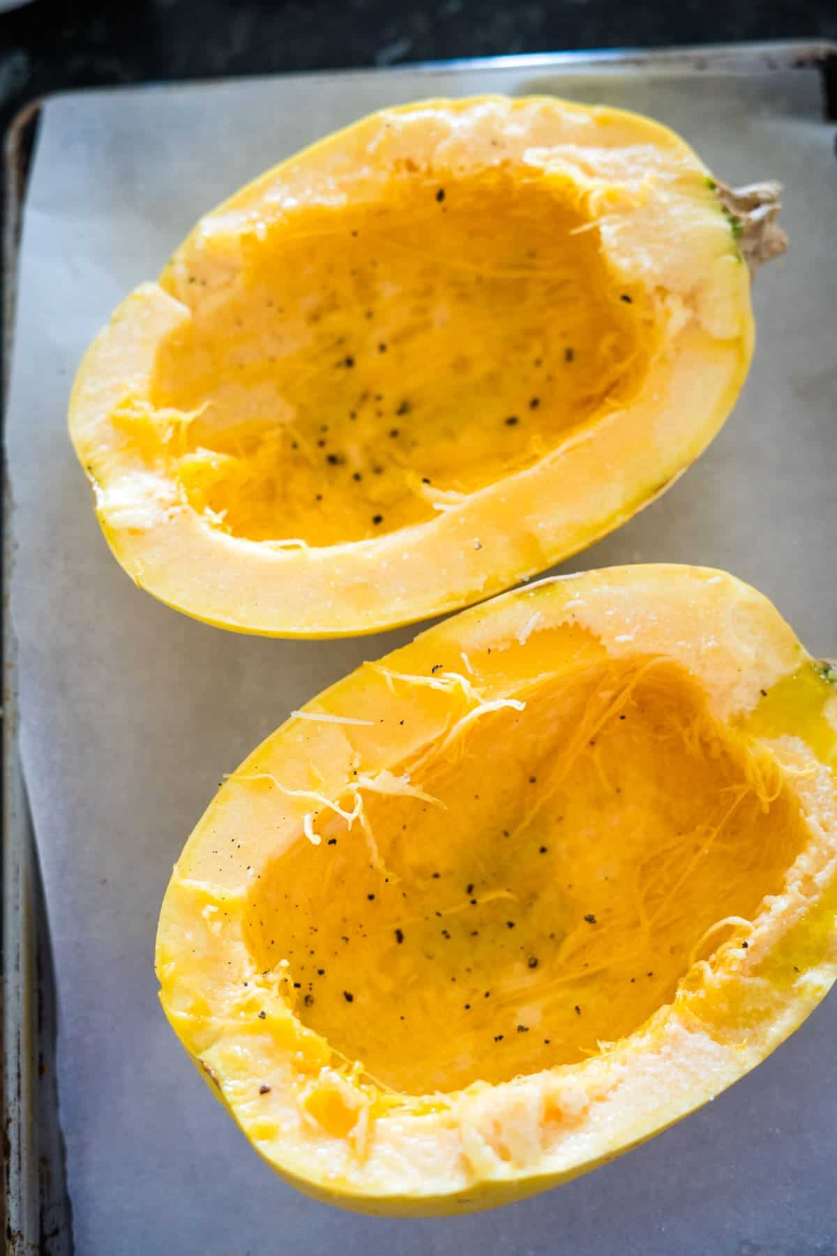 Halved spaghetti squash on a baking sheet, seasoned with salt and pepper.