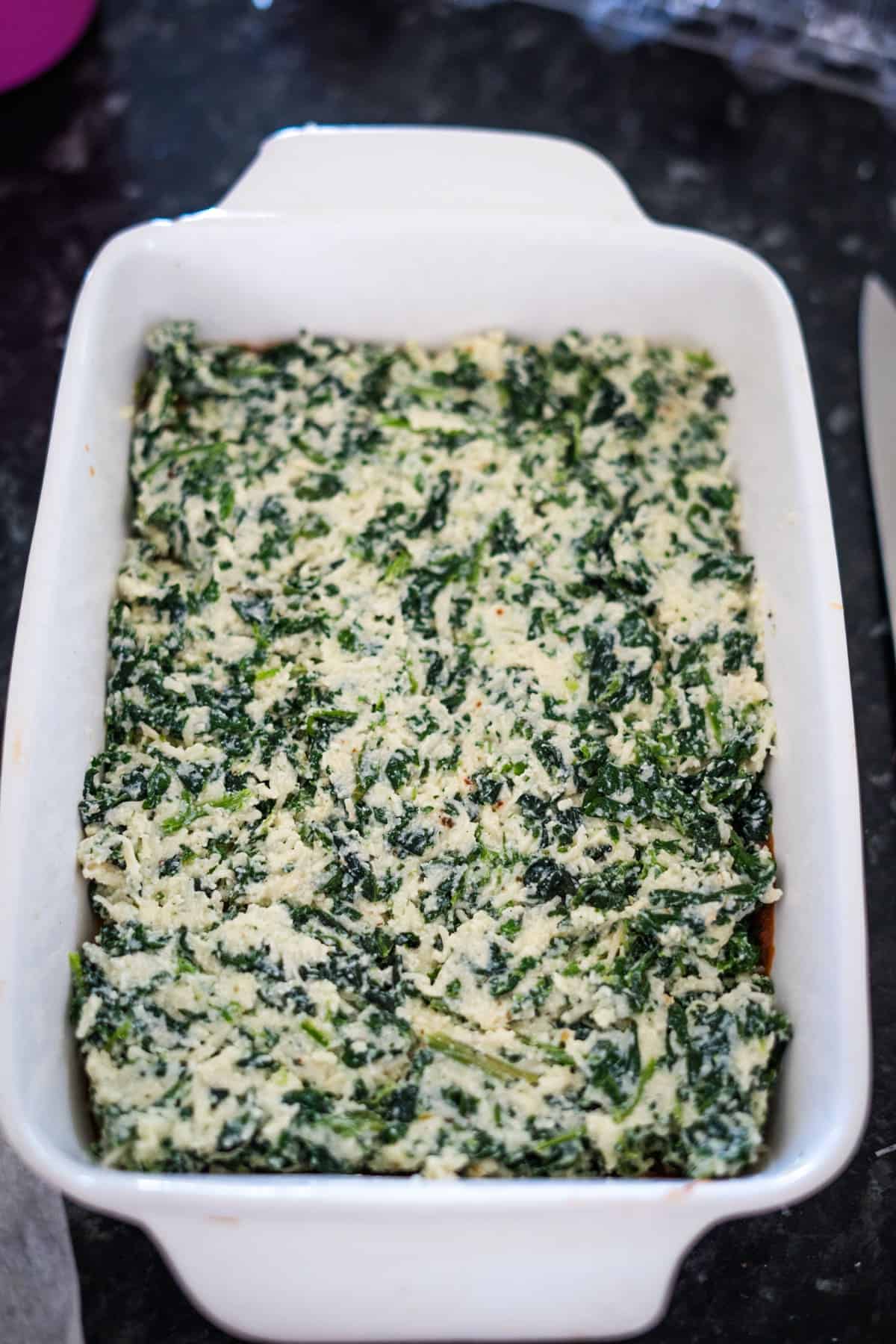 A white baking dish filled with a creamy spinach and cheese mixture, perfectly prepped for a keto spinach lasagna delight.