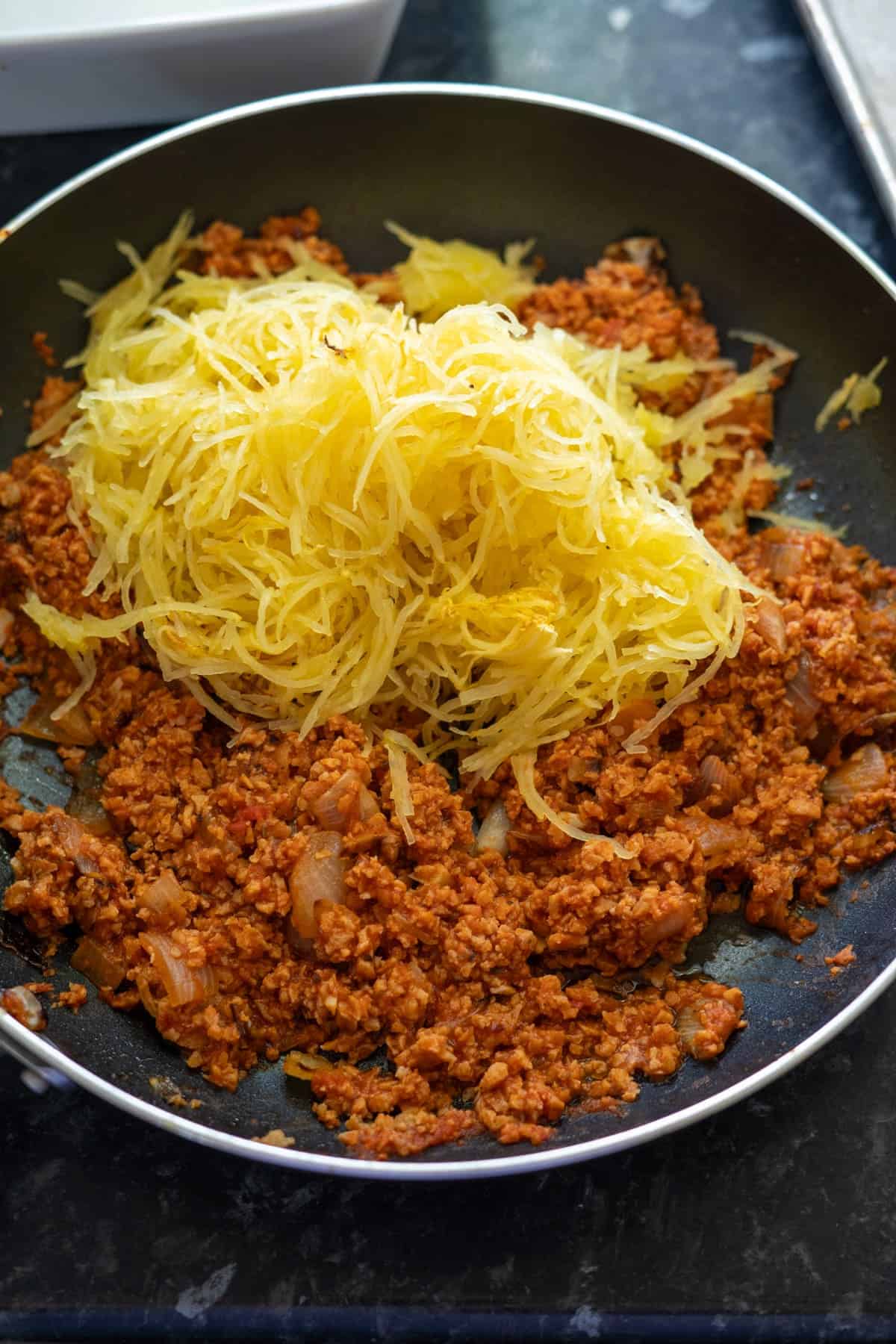 Skillet with cooked ground meat and a pile of shredded spaghetti squash on top.