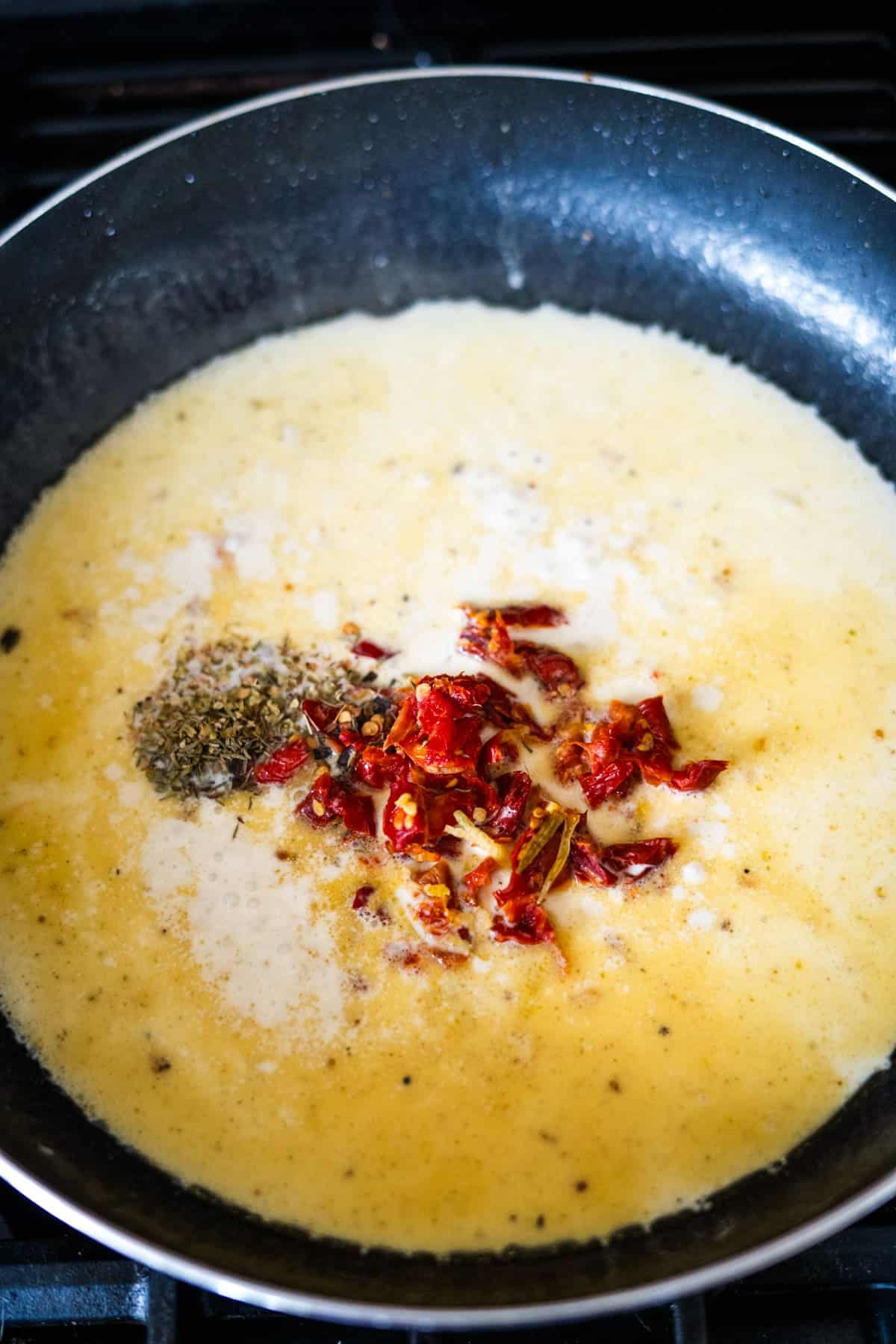 A pan on the stove with a creamy sauce, topped with dried tomatoes and herbs.