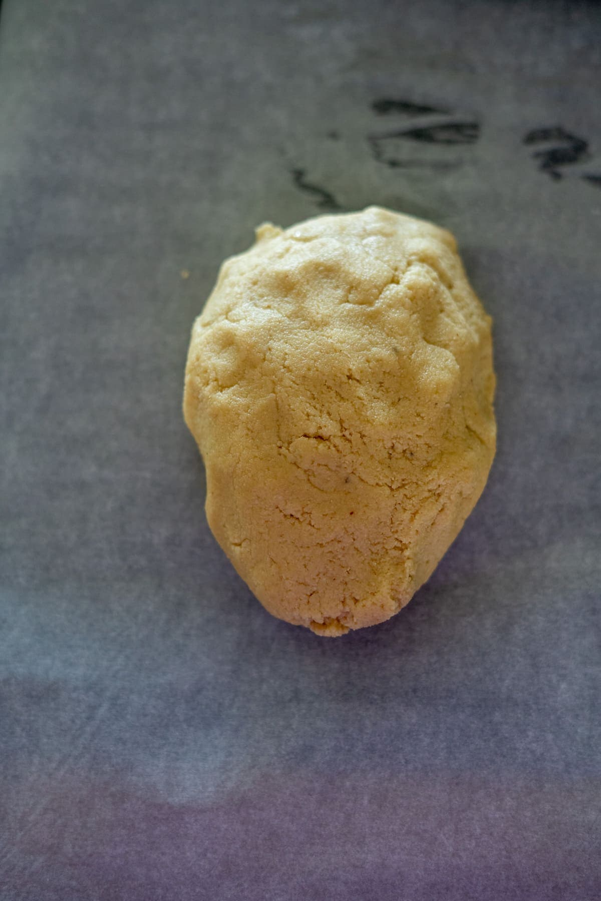 A single ball of uncooked keto dough sits on a sheet of parchment paper, reminiscent of a classic Twix treat.