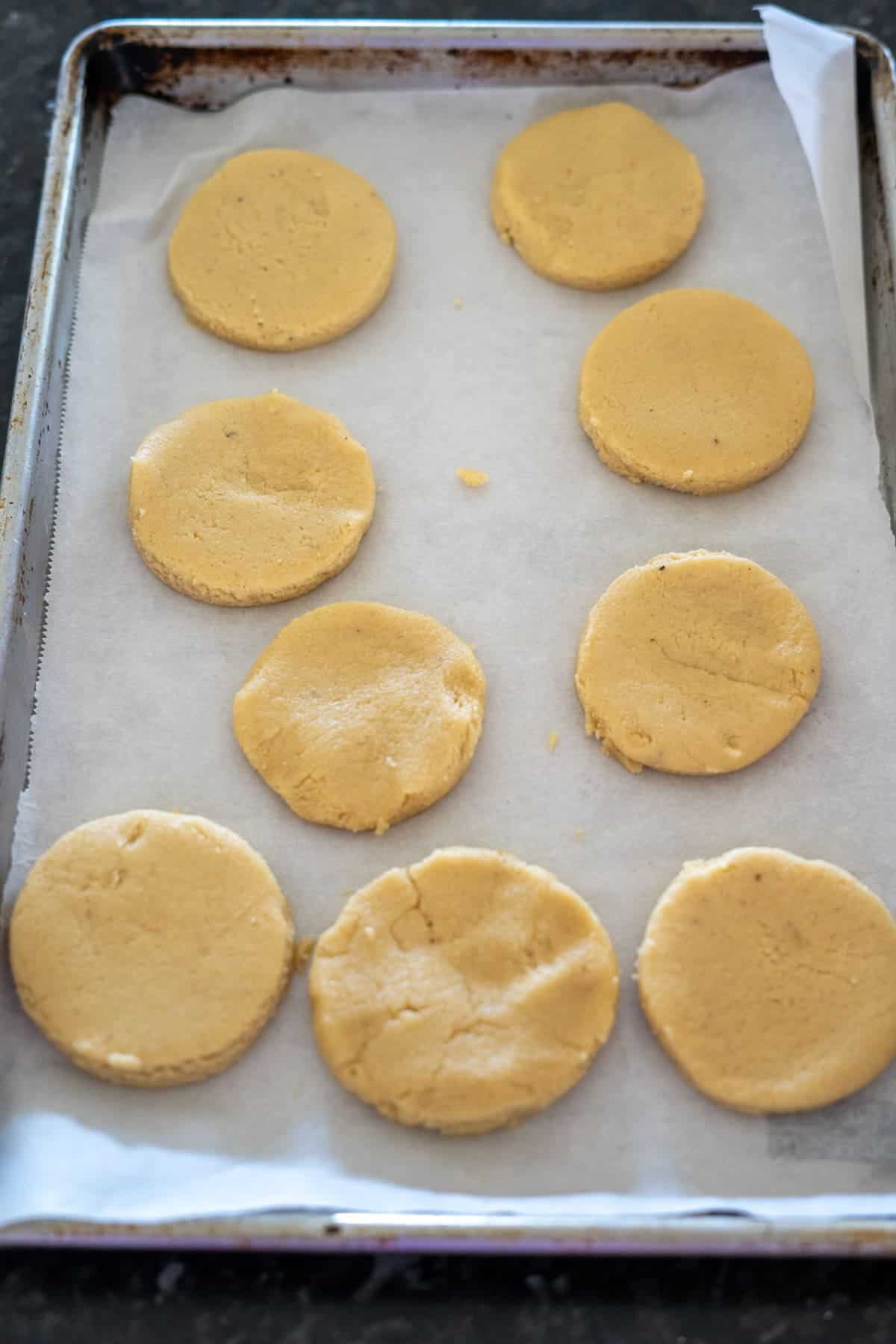 A baking sheet with nine unbaked keto twix cookies rests on a layer of parchment paper, each round delight promising a guilt-free indulgence.