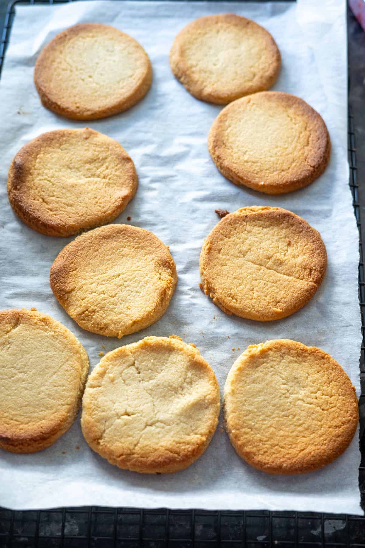 Eight round almond flour linzer cookies rest on parchment paper, cooling on a wire rack.