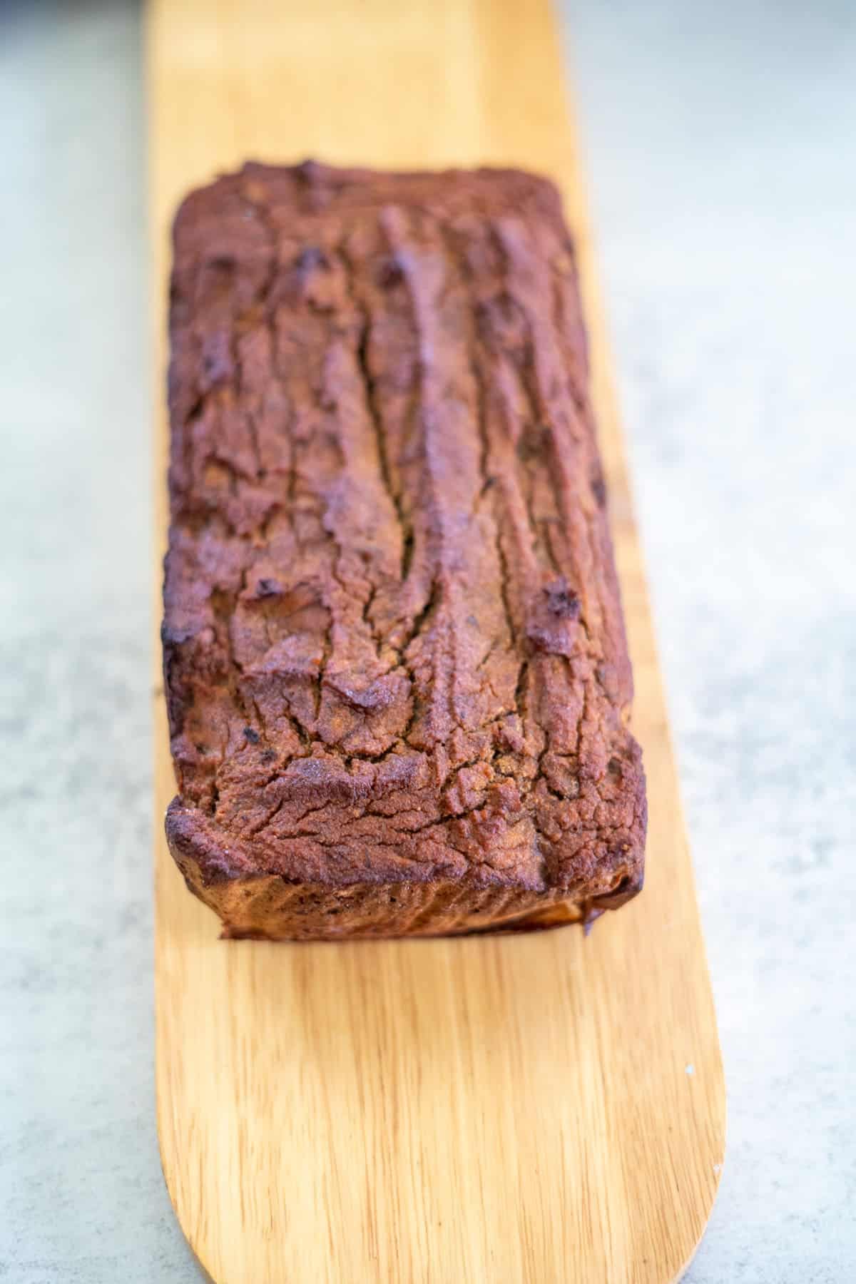 A loaf of banana bread, warm and inviting, rests on a wooden board, the perfect companion to a slice of pumpkin biscotti.