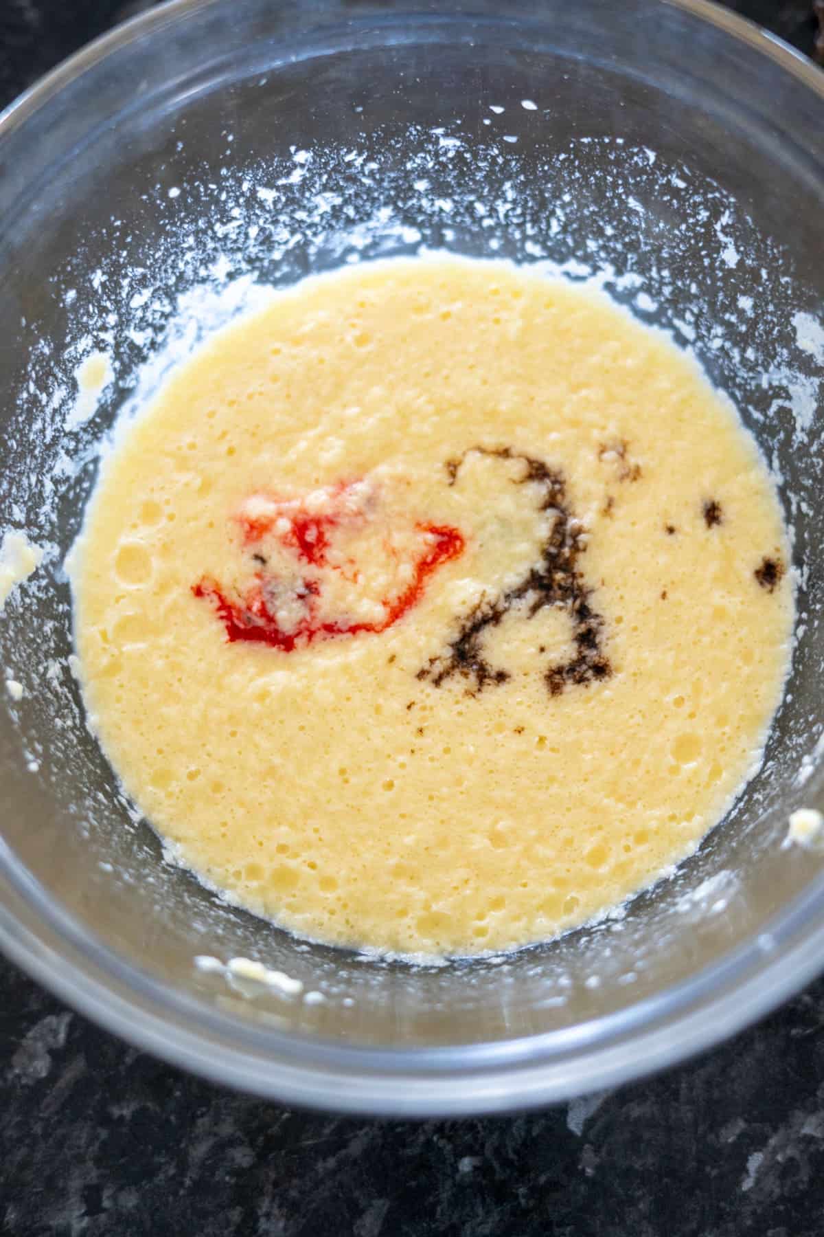 A mixing bowl containing a yellow batter with red and brown ingredients partially blended in.