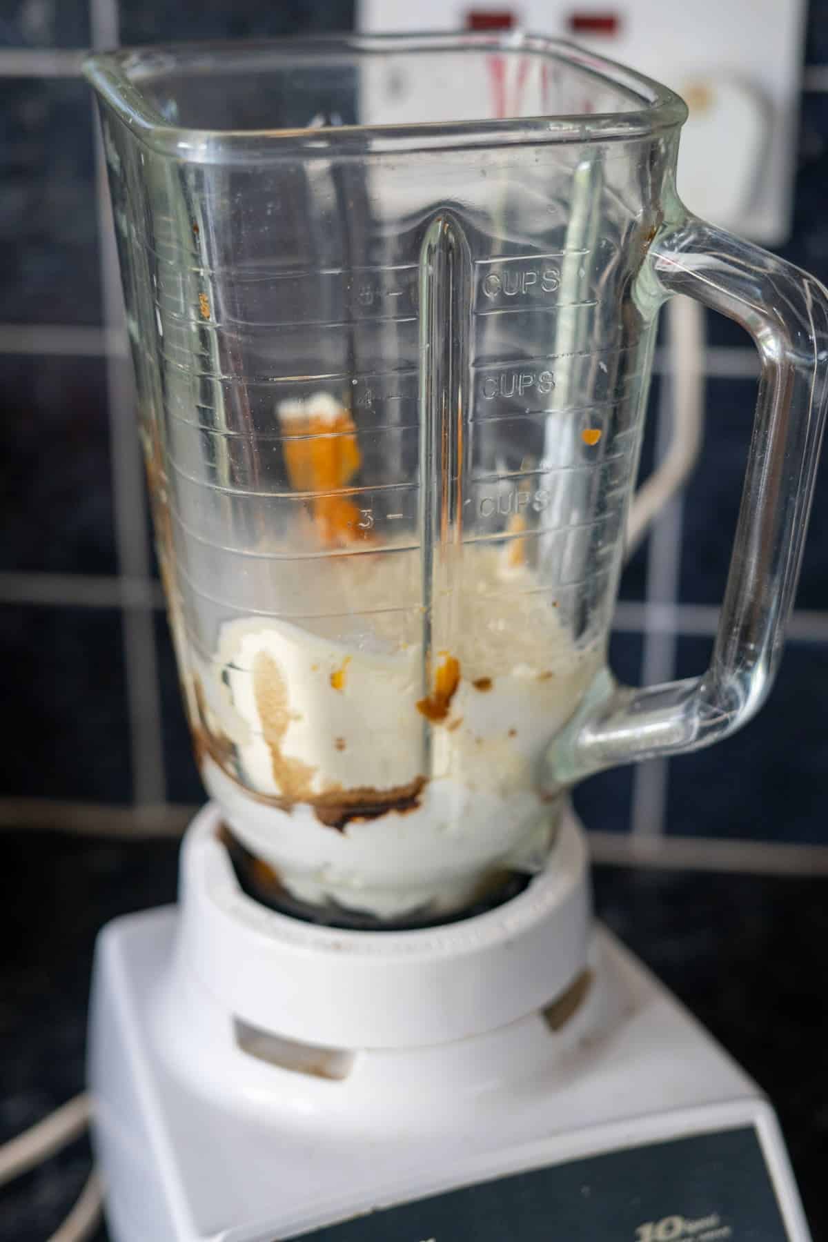 A blender with a mixture of yogurt, peanut butter, and liquid ingredients inside, on a kitchen counter.