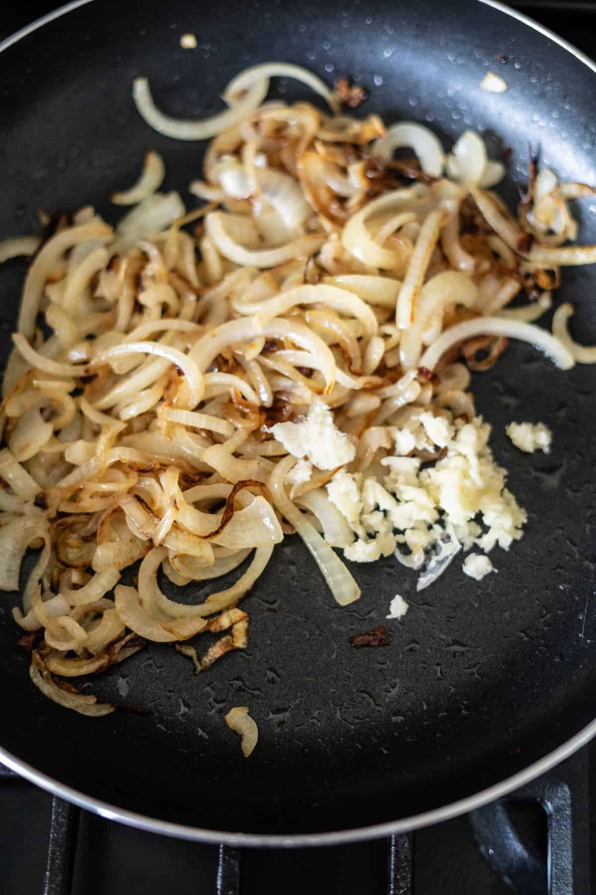 Sliced onions and minced garlic cooking in a black frying pan on a stove.