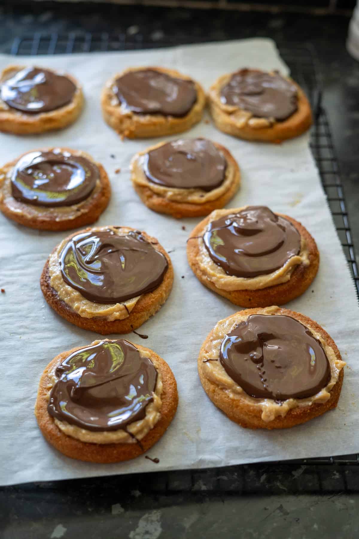 Keto Twix-inspired cookies with peanut butter and chocolate spread rest on a cooling rack lined with parchment paper.