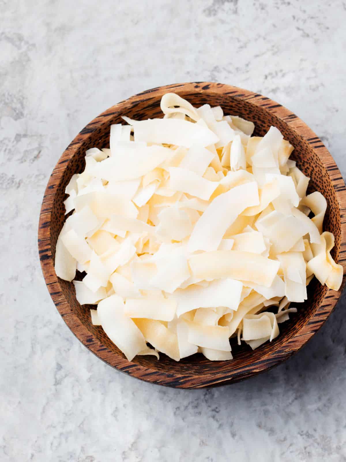 A wooden bowl brimming with wide, flat, ivory-colored pasta ribbons rests on a light textured surface, evoking a sense of culinary wanderlust akin to discovering new keto travel snacks.