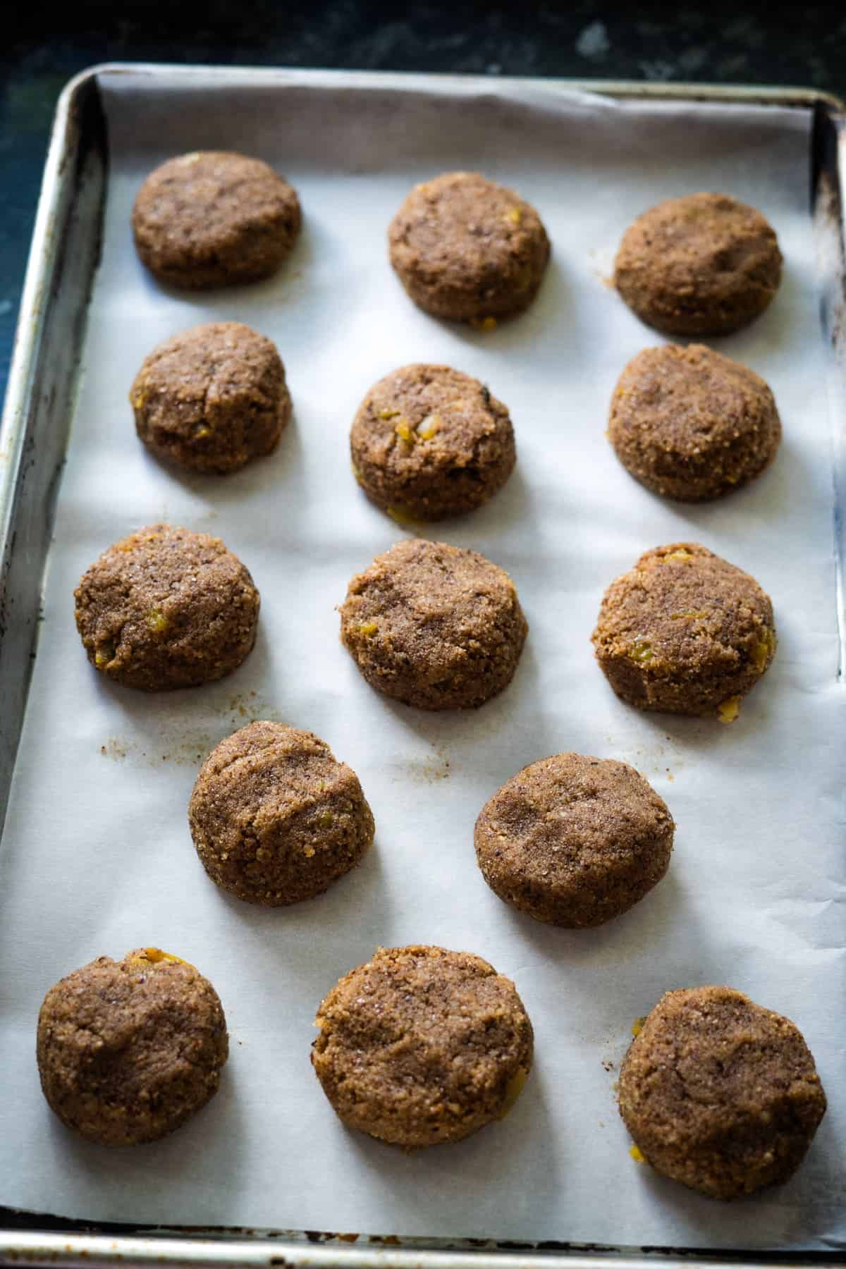 Fifteen round, low-carb lebkuchen cookies are arranged on a parchment-lined baking sheet.