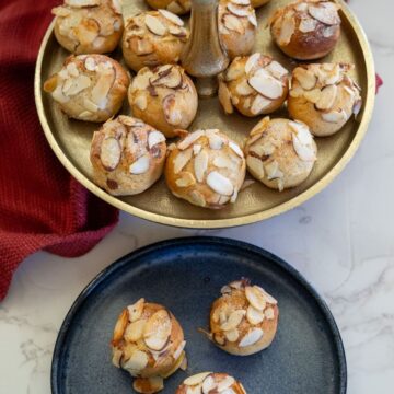 Two-tiered tray with almond cookies on top, one cookie on a separate blue plate. Red cloth in the background.