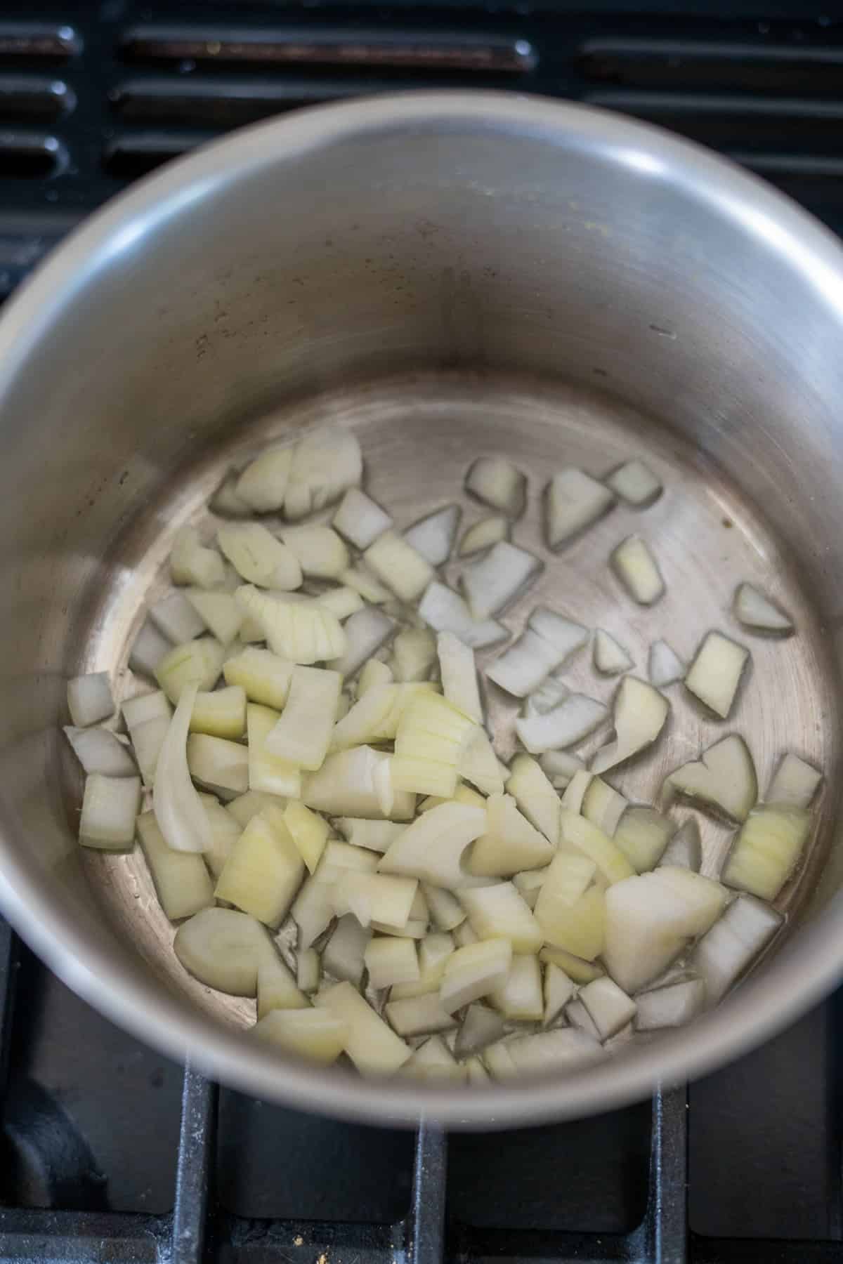 Chopped onions in a metal saucepan on a stovetop.