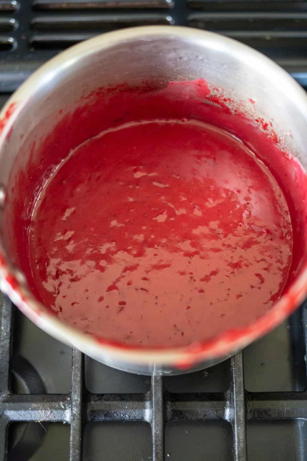 A pot filled with a smooth red sauce sits on a black stovetop grate.