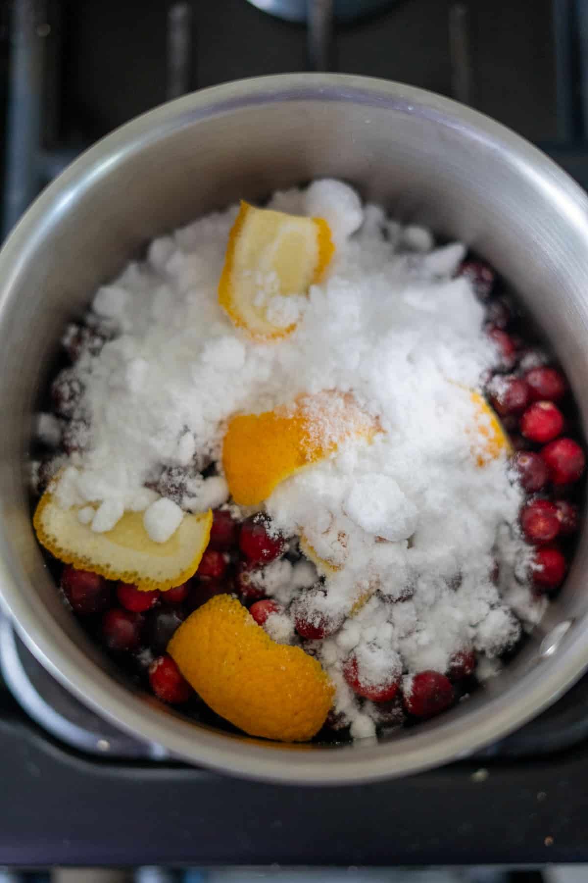 Cranberries, orange peels, and sugar in a pot on a stove.