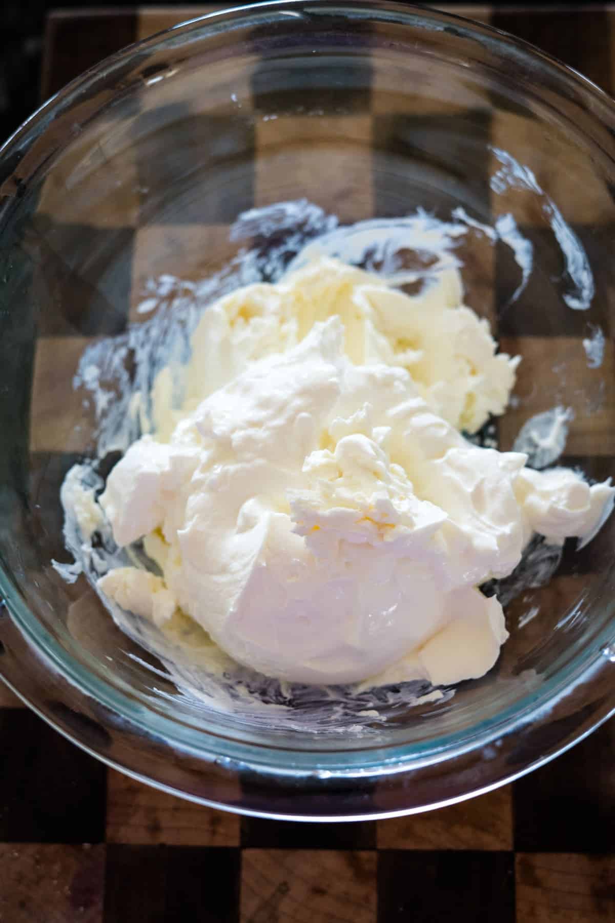 A glass bowl containing whipped cream on a wooden surface.