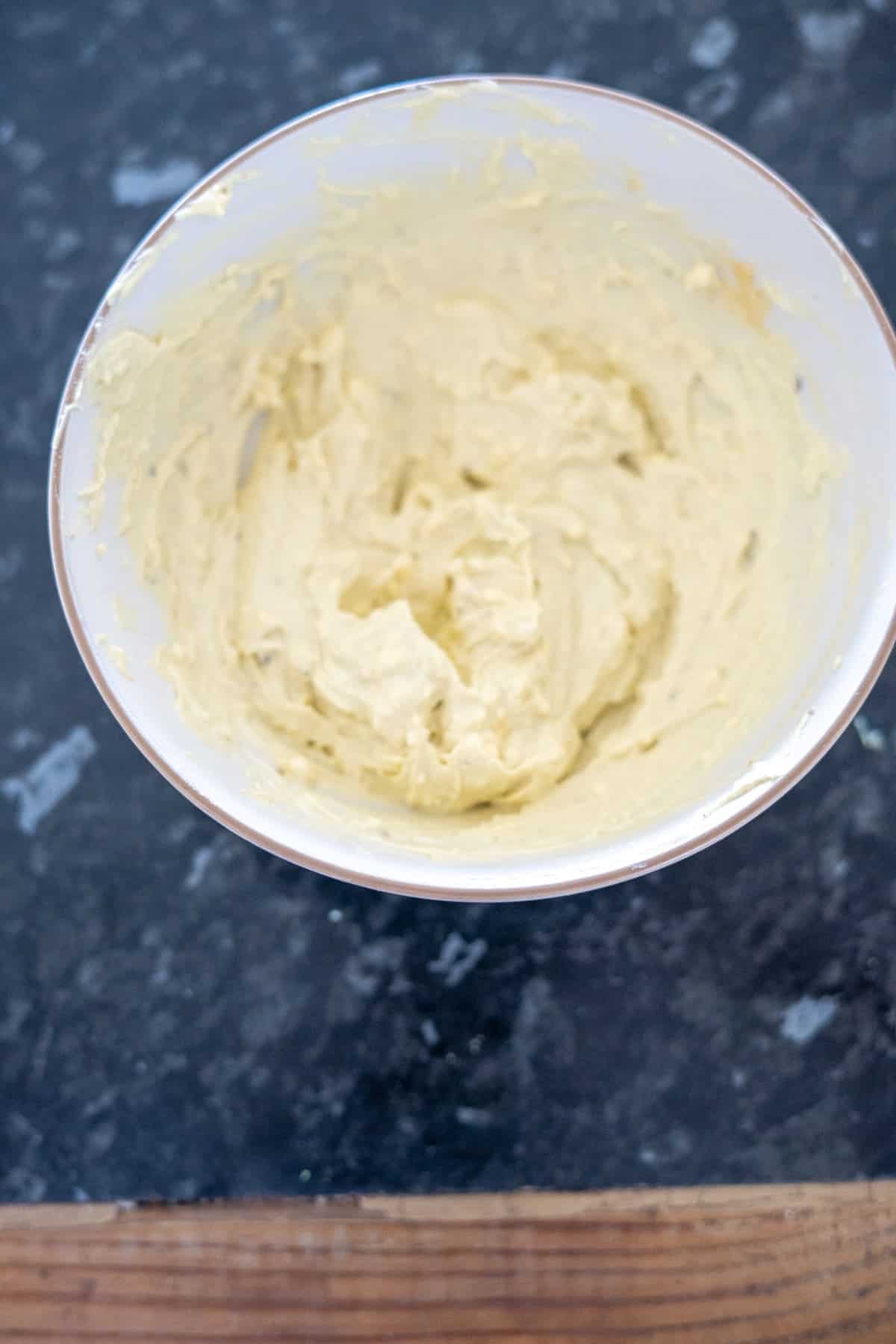 A bowl of yellowish, creamy butter sits on a dark countertop, reminiscent of the rich texture found in perfectly crafted keto deviled eggs.