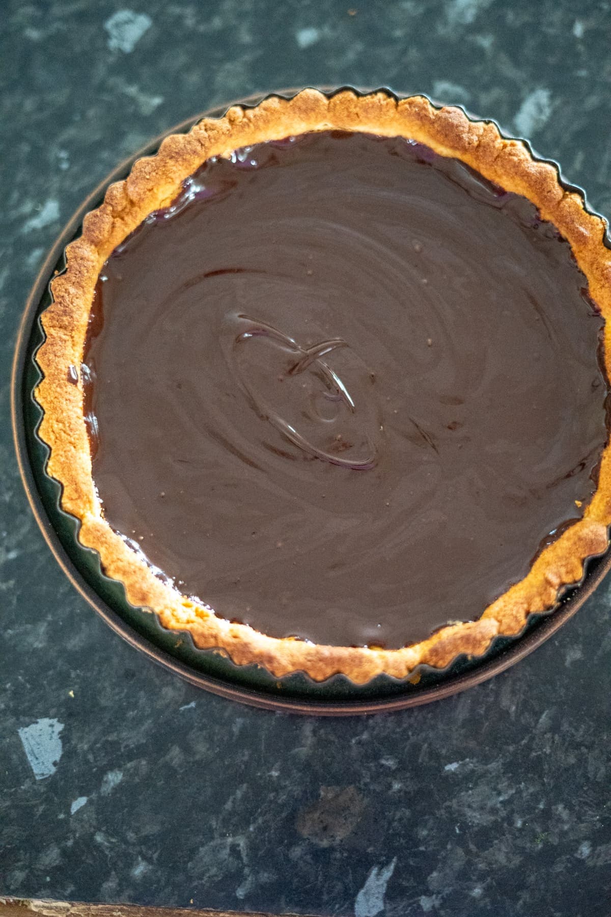 A keto chocolate tart with a smooth, glossy surface sits enticingly on a dark countertop.