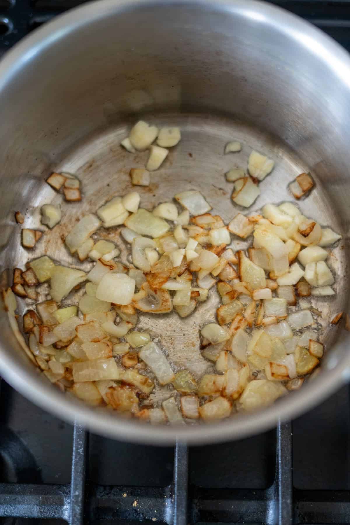 Chopped onions sautéing in a stainless steel pan on a stovetop.