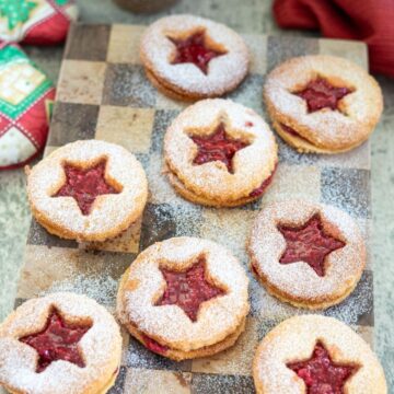 Star-shaped Linzer cookies with raspberry filling and powdered sugar on a wooden board.