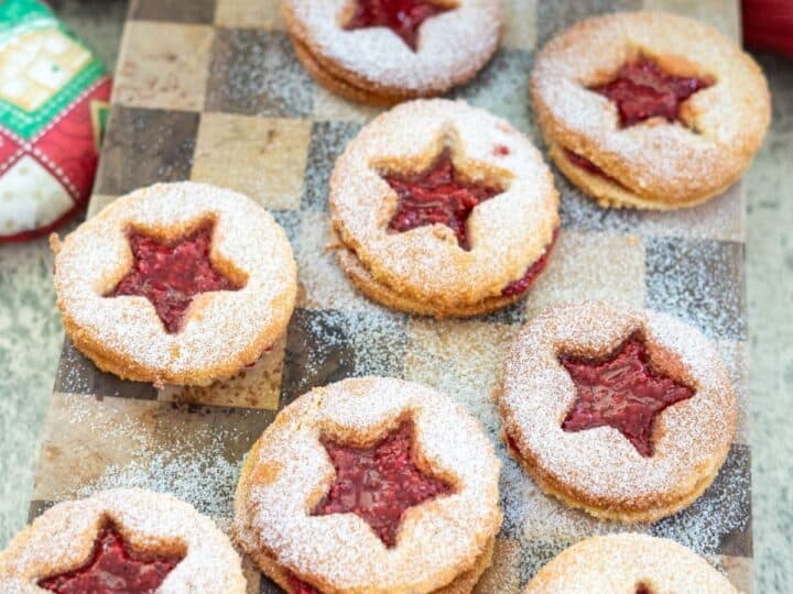 Star-shaped Linzer cookies with raspberry filling and powdered sugar on a wooden board.