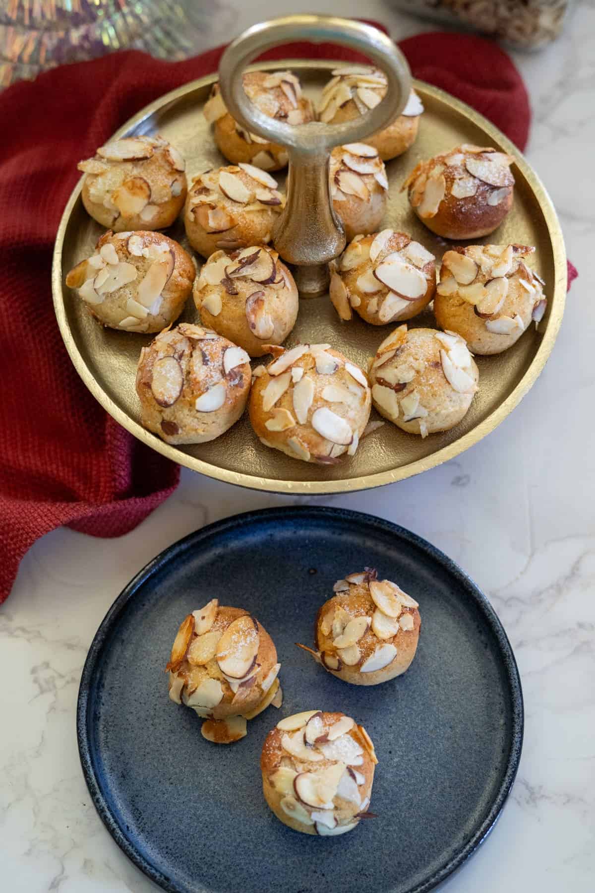 A tray showcasing almond-topped pastries rests elegantly on a marble surface, accompanied by three delicate almond cookies arranged on a sleek black plate below.