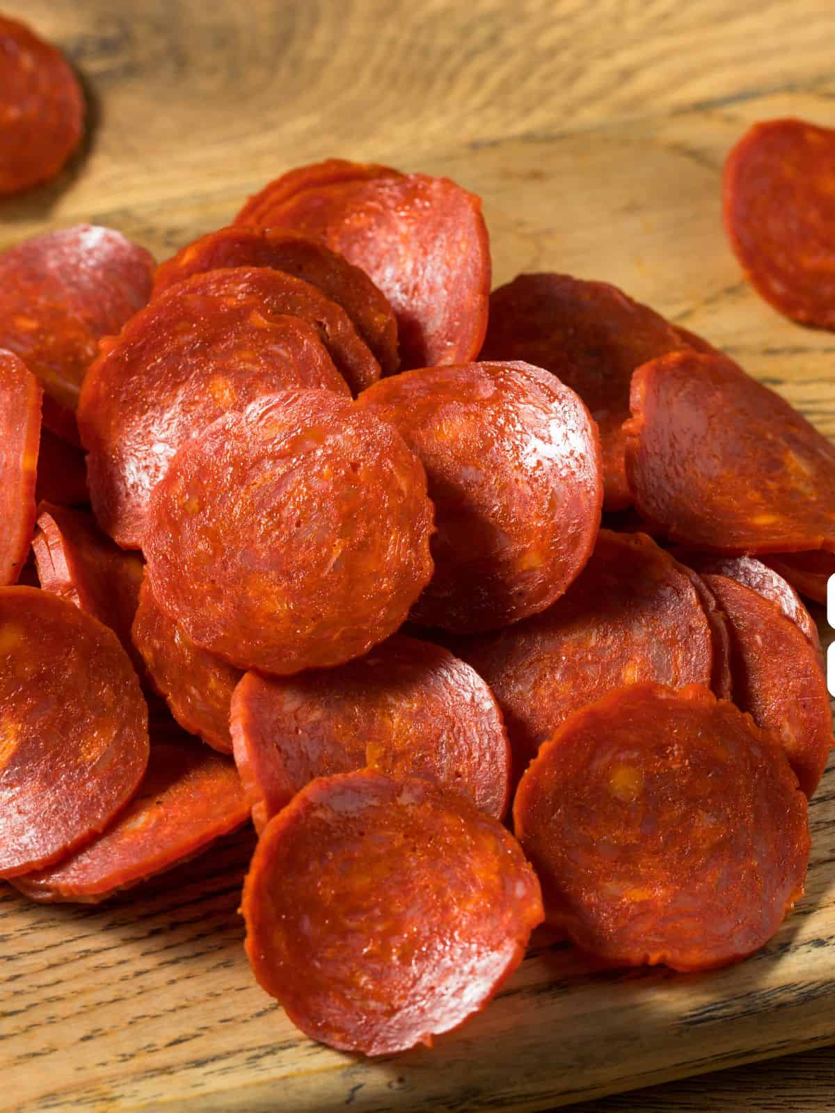 A pile of pepperoni slices on a wooden surface, perfect as keto travel snacks.