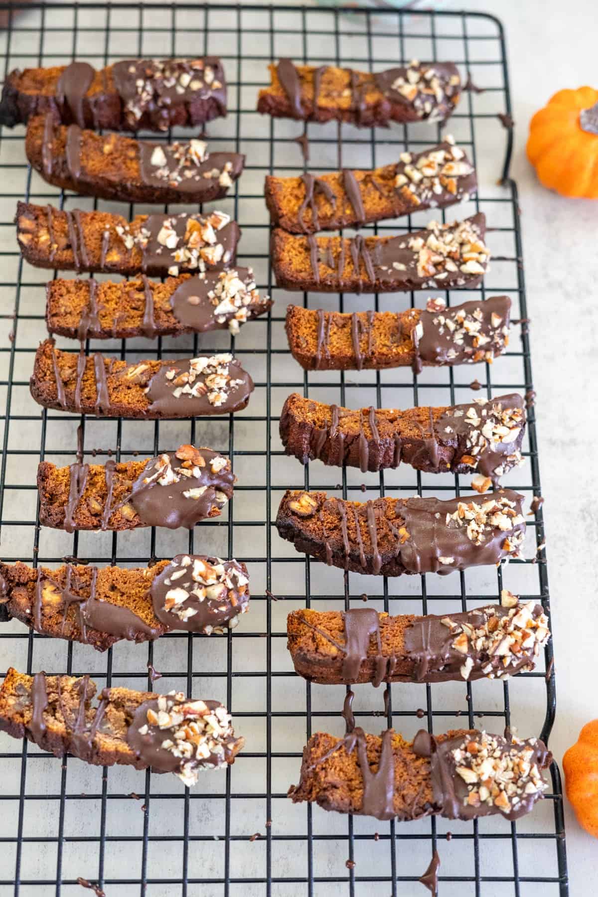 Biscotti topped with chocolate and nuts are arranged on a cooling rack.