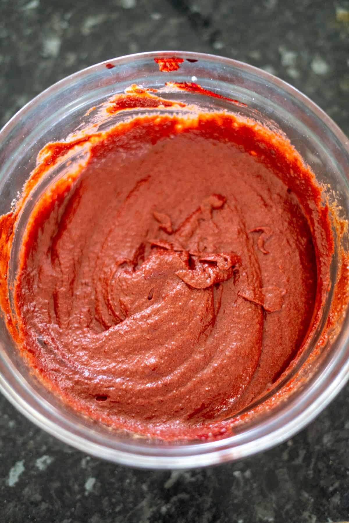 A small container filled with smooth, red gochujang paste on a dark surface.