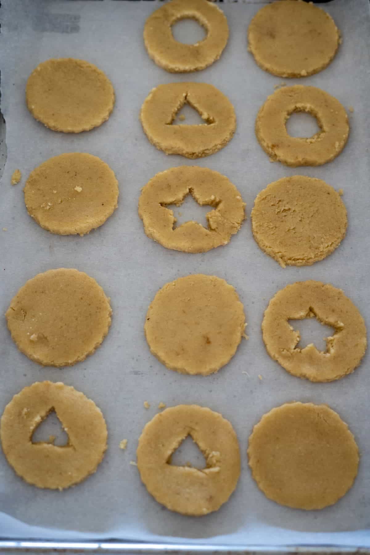 Almond flour Linzer cookies, cut into circular shapes with triangle and star cutouts, are artfully arranged on parchment paper.