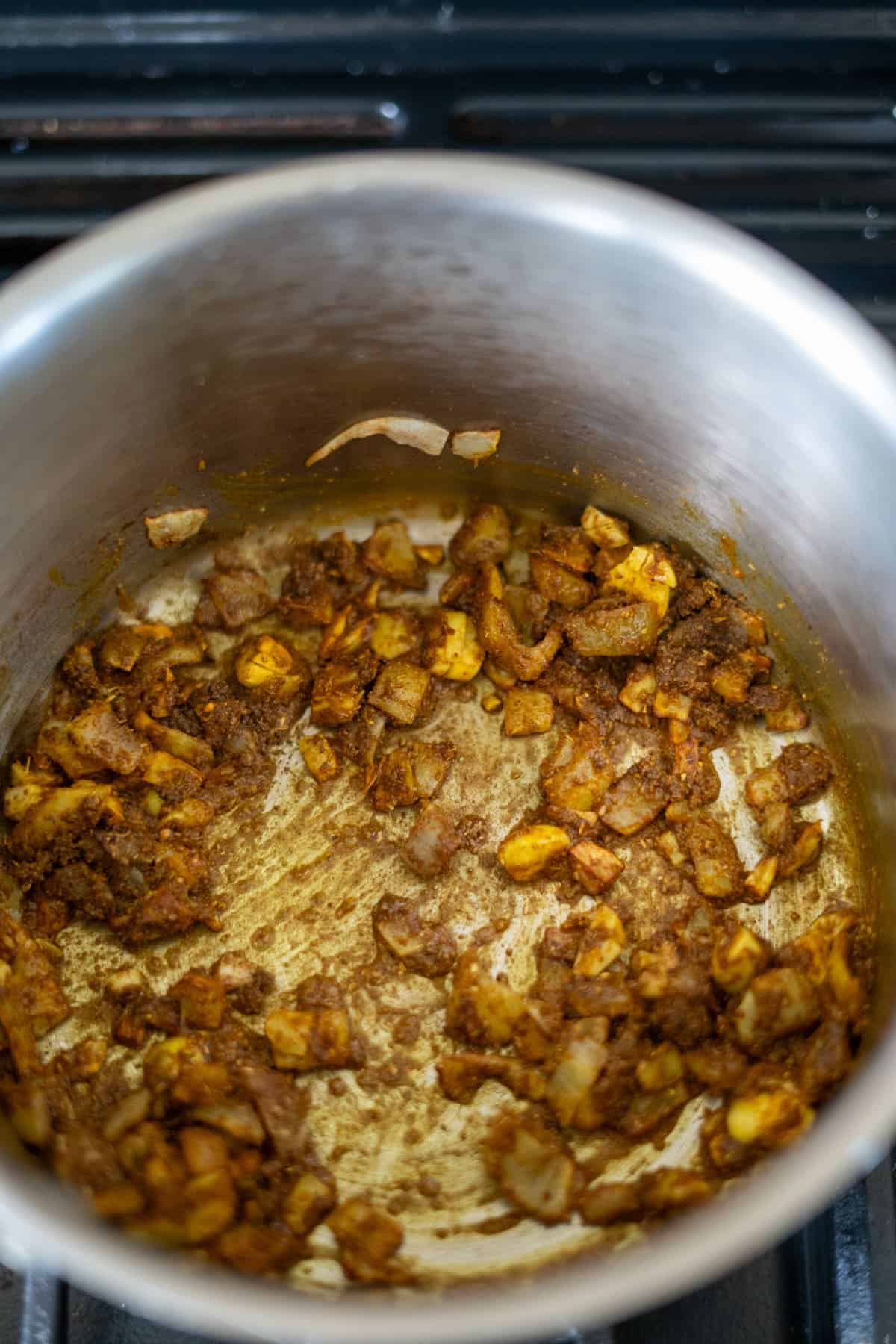 Chopped onions and spices being sautéed in a stainless steel pot.