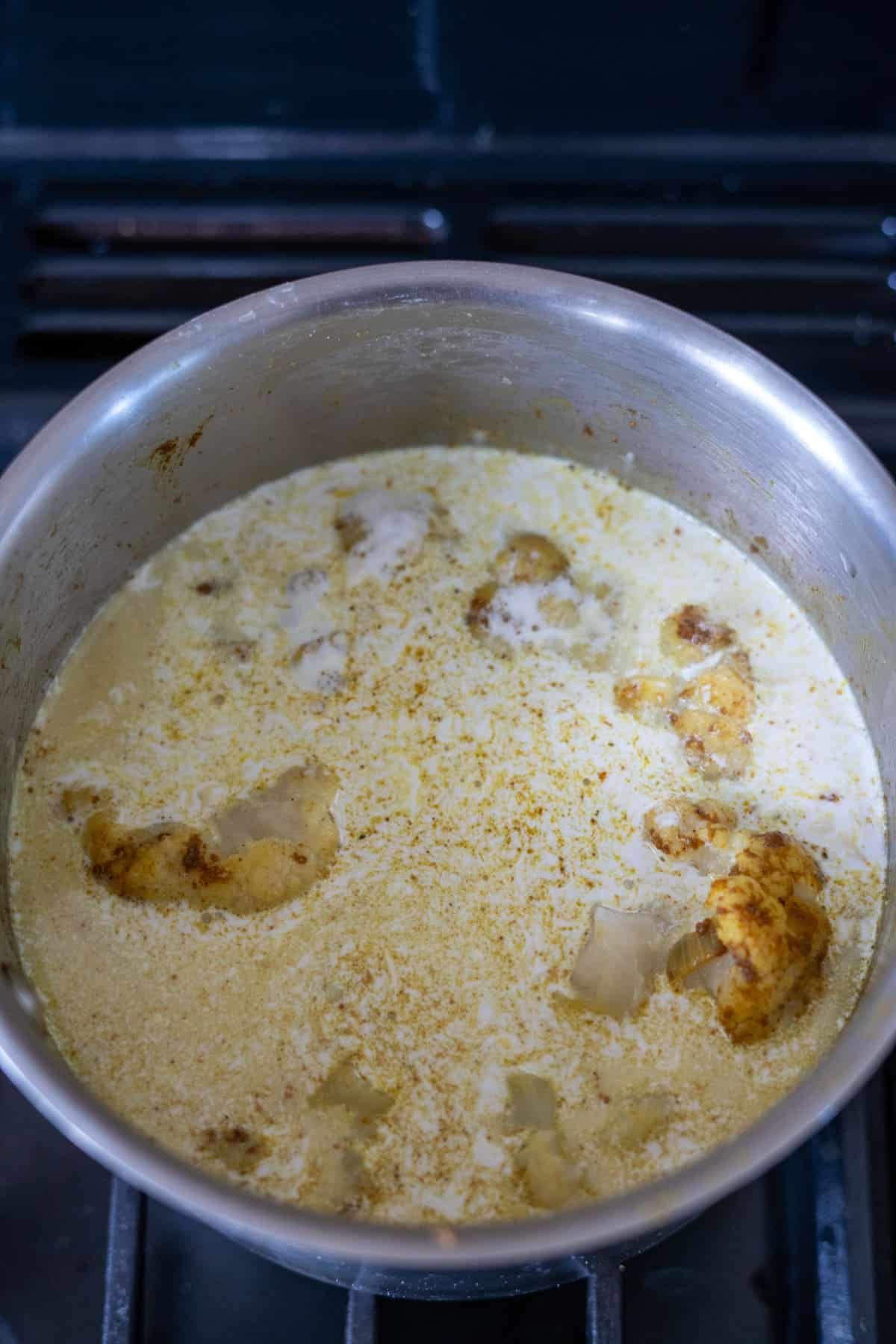 A pot on a stove containing a creamy curry with visible pieces of cauliflower.