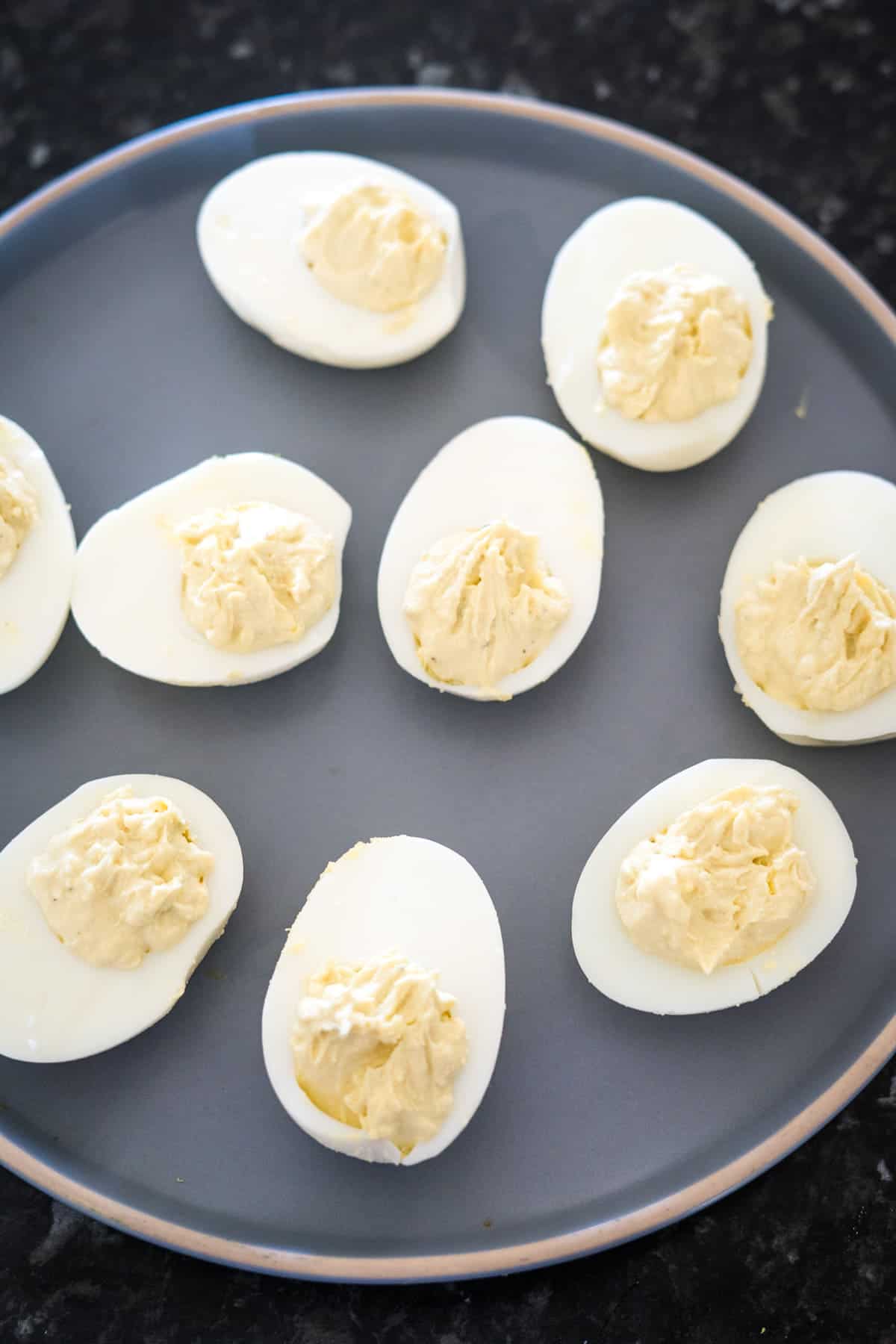 Plate with nine keto deviled eggs, each boasting a creamy filling, on a dark surface.