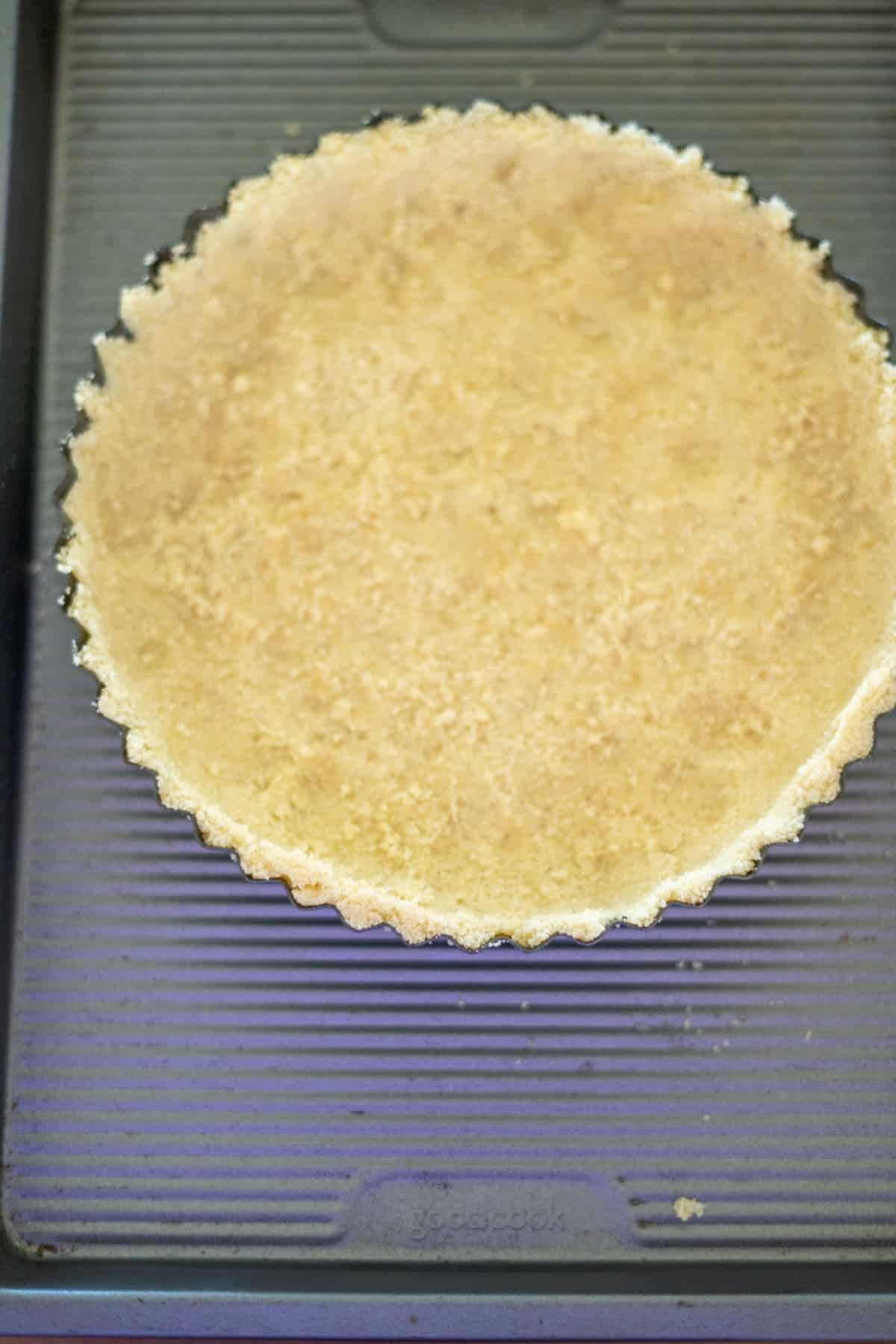 A round pie crust in a fluted tart pan on a baking tray.